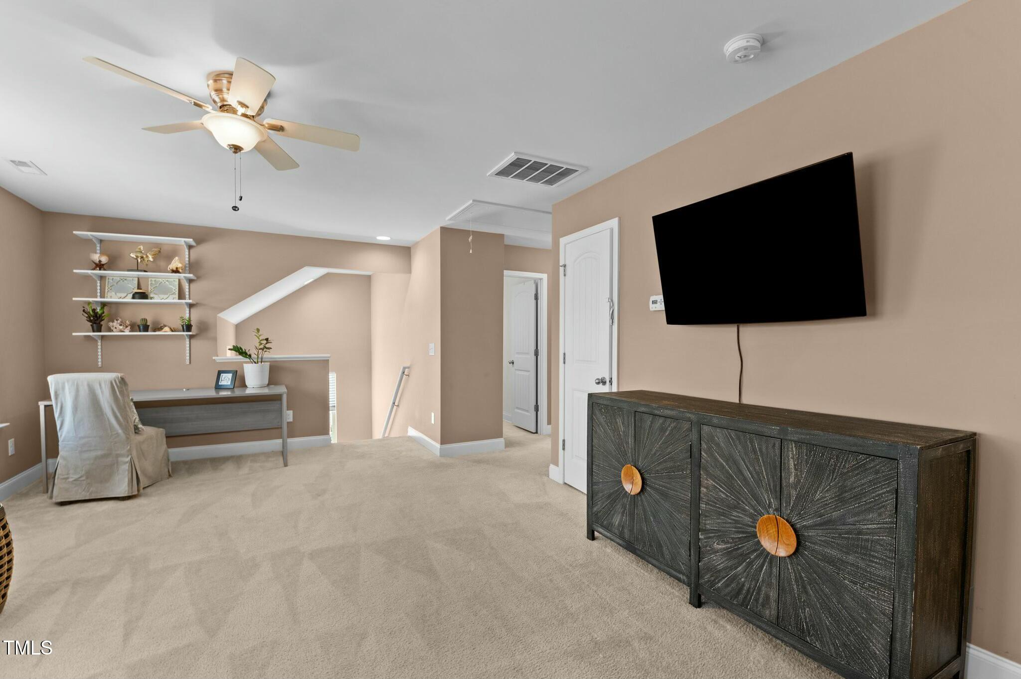 Furnished bonus room with a wall-mounted TV, dark cabinet, ceiling fan, and desk nook.