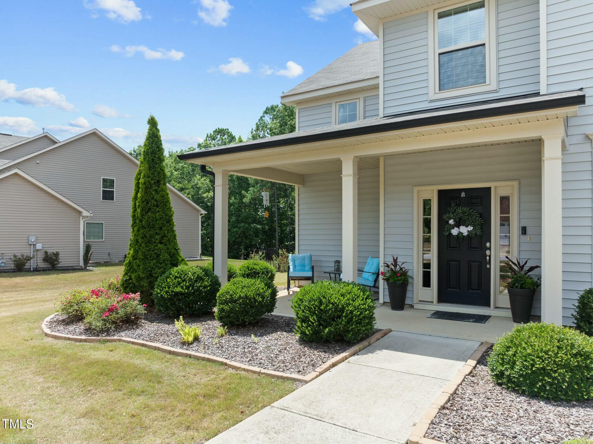 Two-story gray home with a covered porch, black front door, blue chairs, and landscaped walkway.
