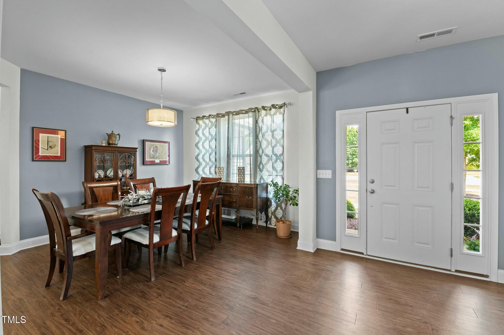 Furnished dining room with a dark wood table beside a white entry door with sidelights.