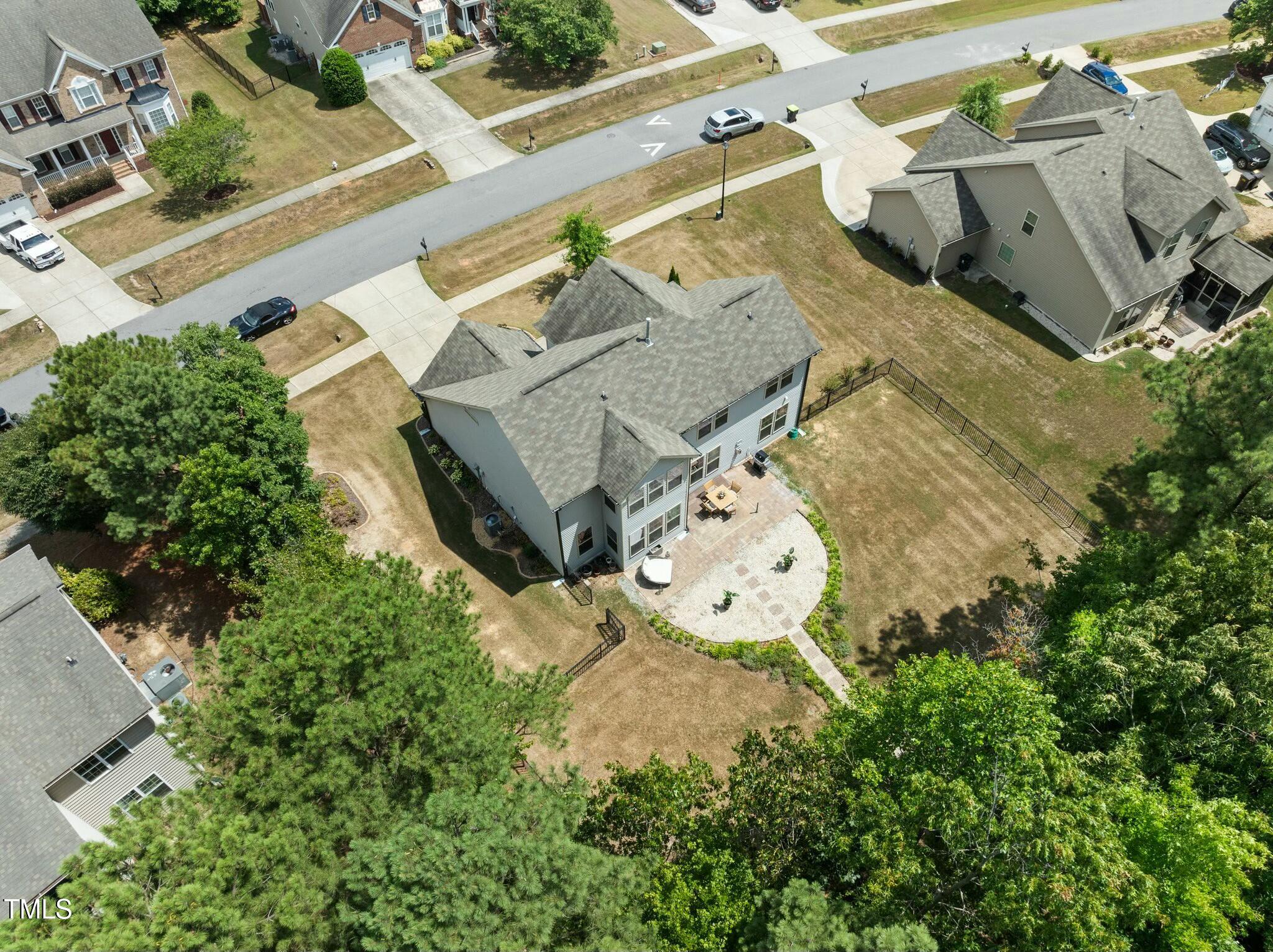 Aerial view of a two-story home with a curved patio and fenced backyard.