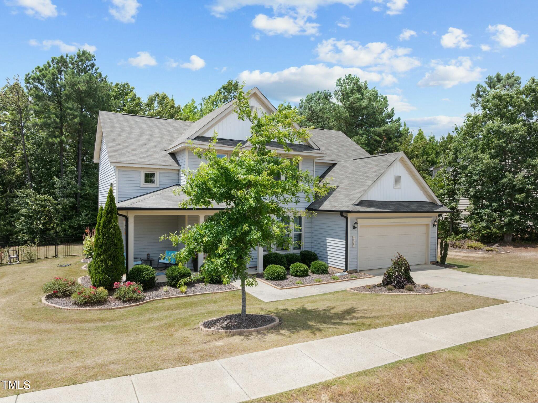 Two-story blue house with a covered porch, attached garage, and landscaped front yard.