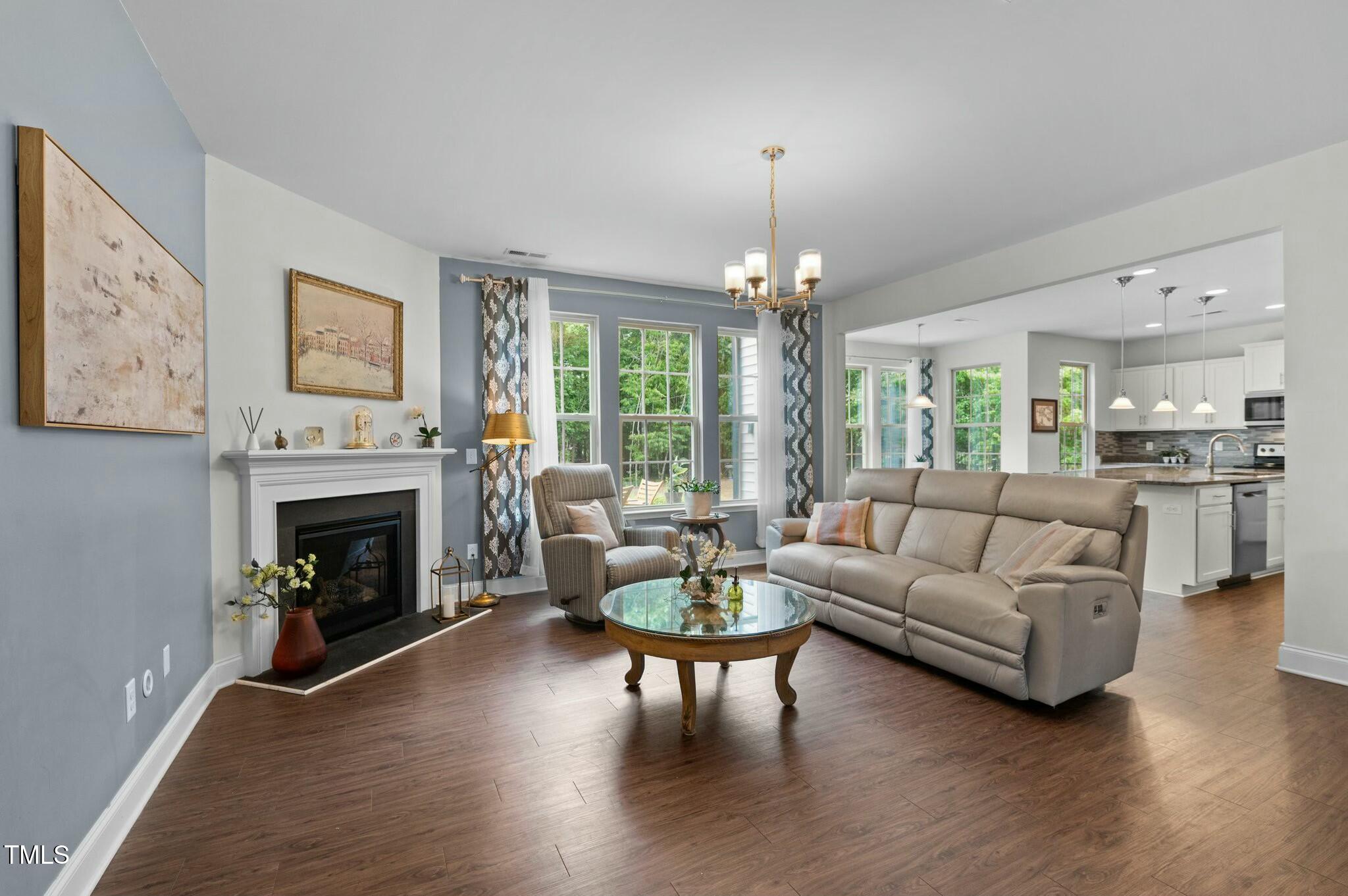 Furnished living room with a fireplace, large windows, and an open kitchen.