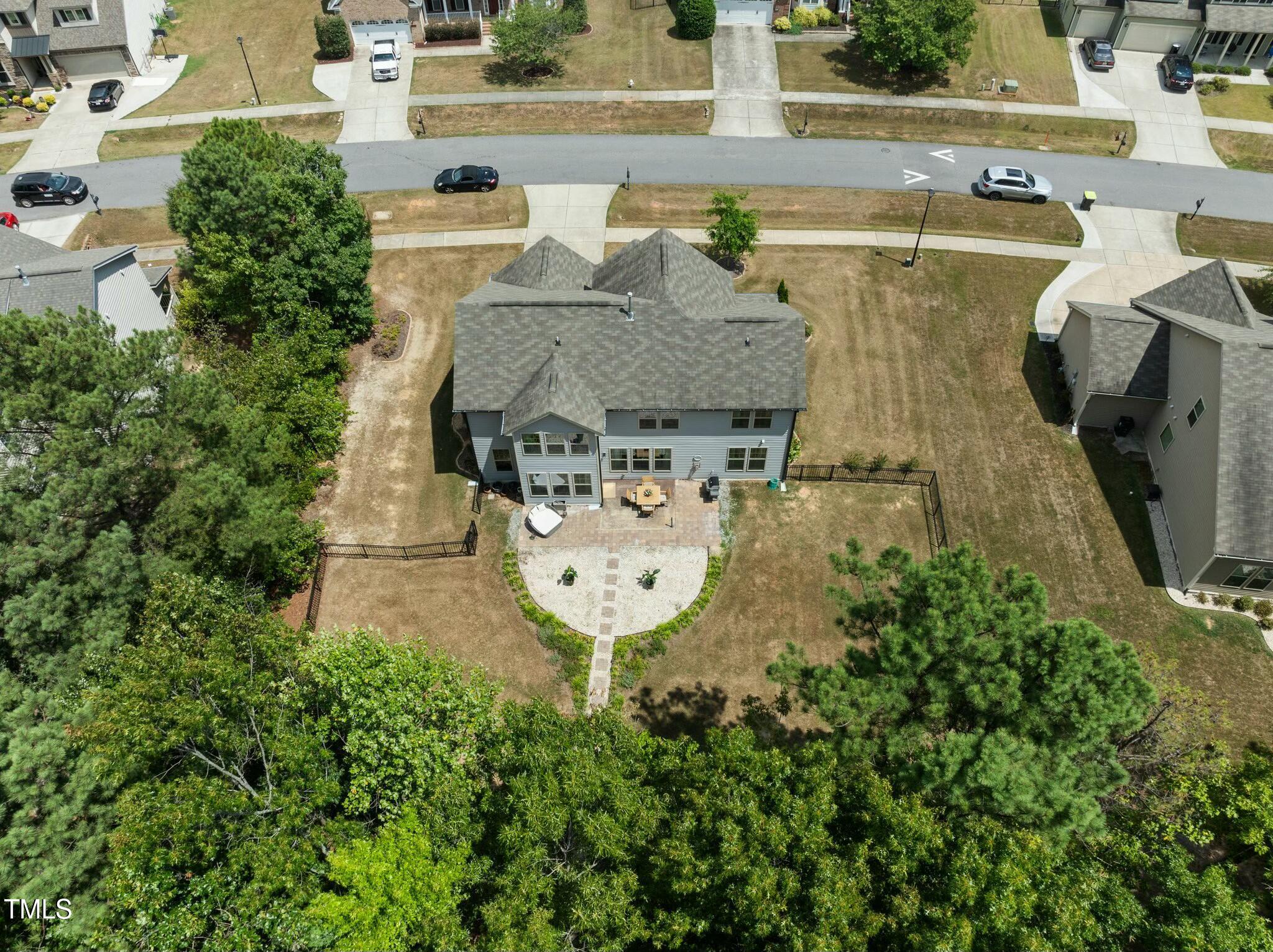 Aerial view of a gray two-story house with a fenced backyard, brick patio, and curved garden path.