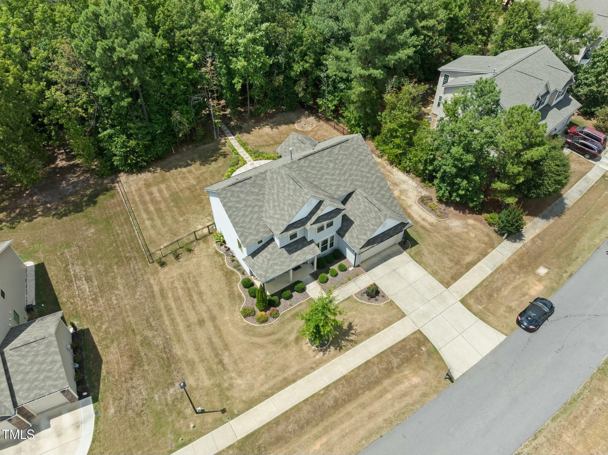 Aerial view of a two-story house with a broad lawn, driveway, and wooded backyard.