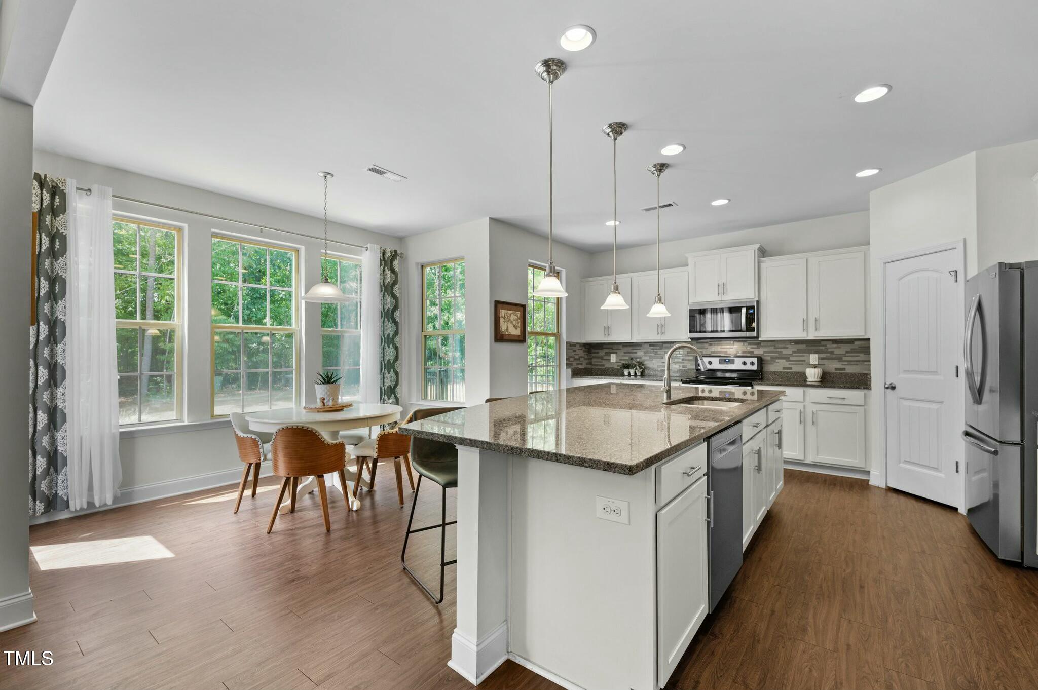 Kitchen with a large granite island, white cabinetry, stainless steel appliances, and a window-side dining nook.