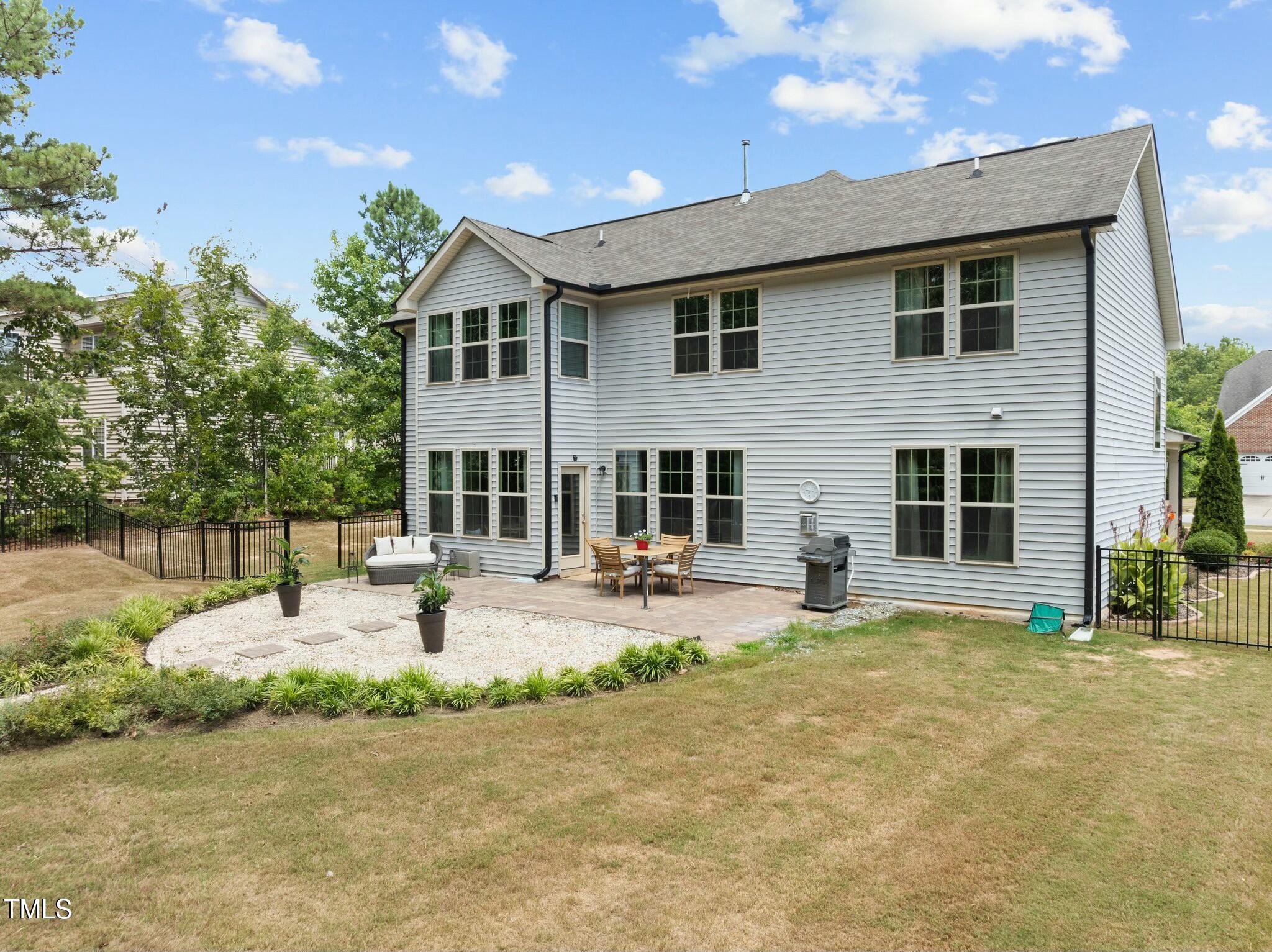 Two-story gray-sided home with a fenced backyard, stone patio, outdoor dining set, and grill.