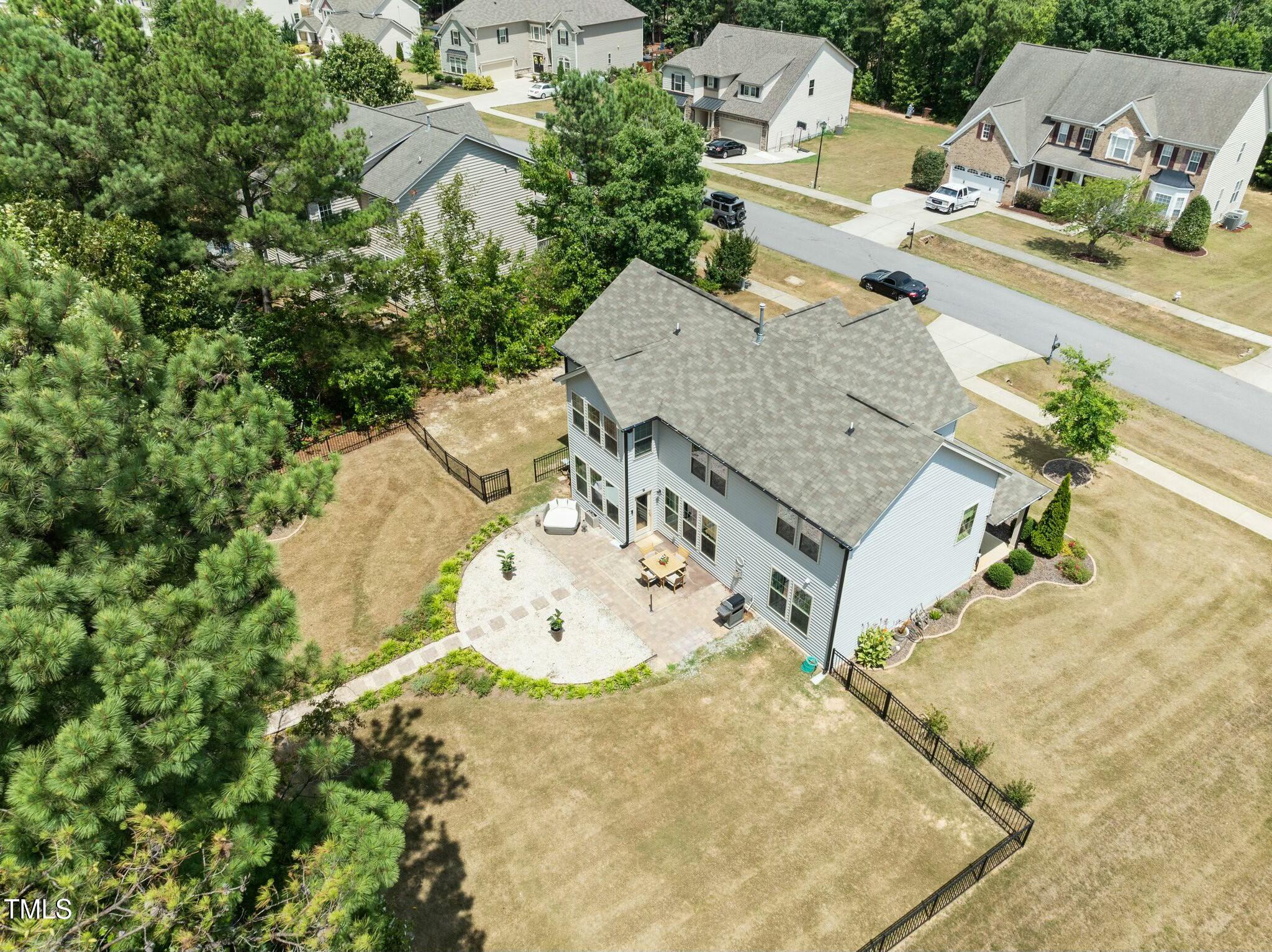 Aerial view of a gray two-story home with a fenced backyard, mature pines, and a patio.