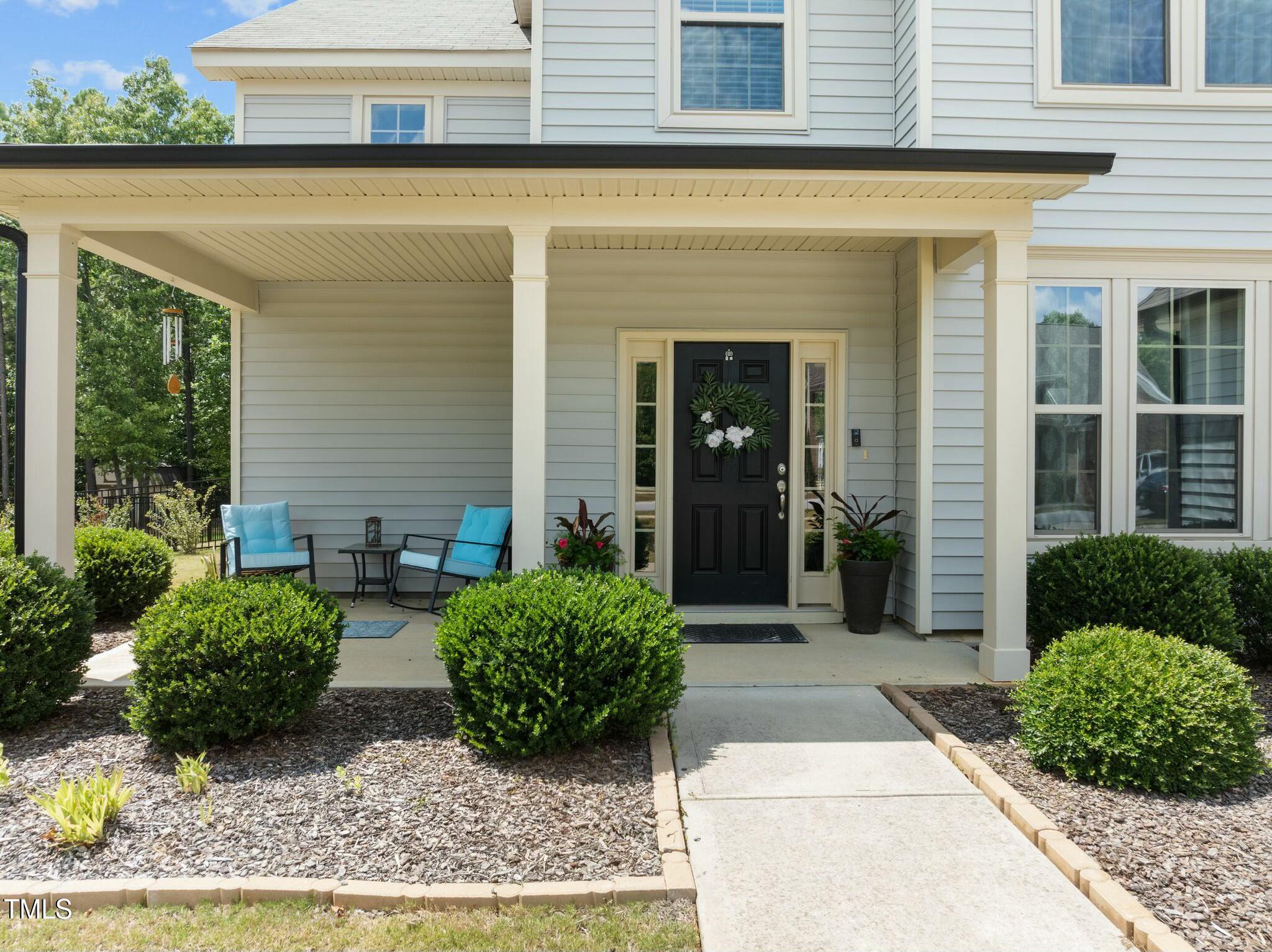 Home entrance with a covered porch, black front door, blue chairs, and landscaped walkway.