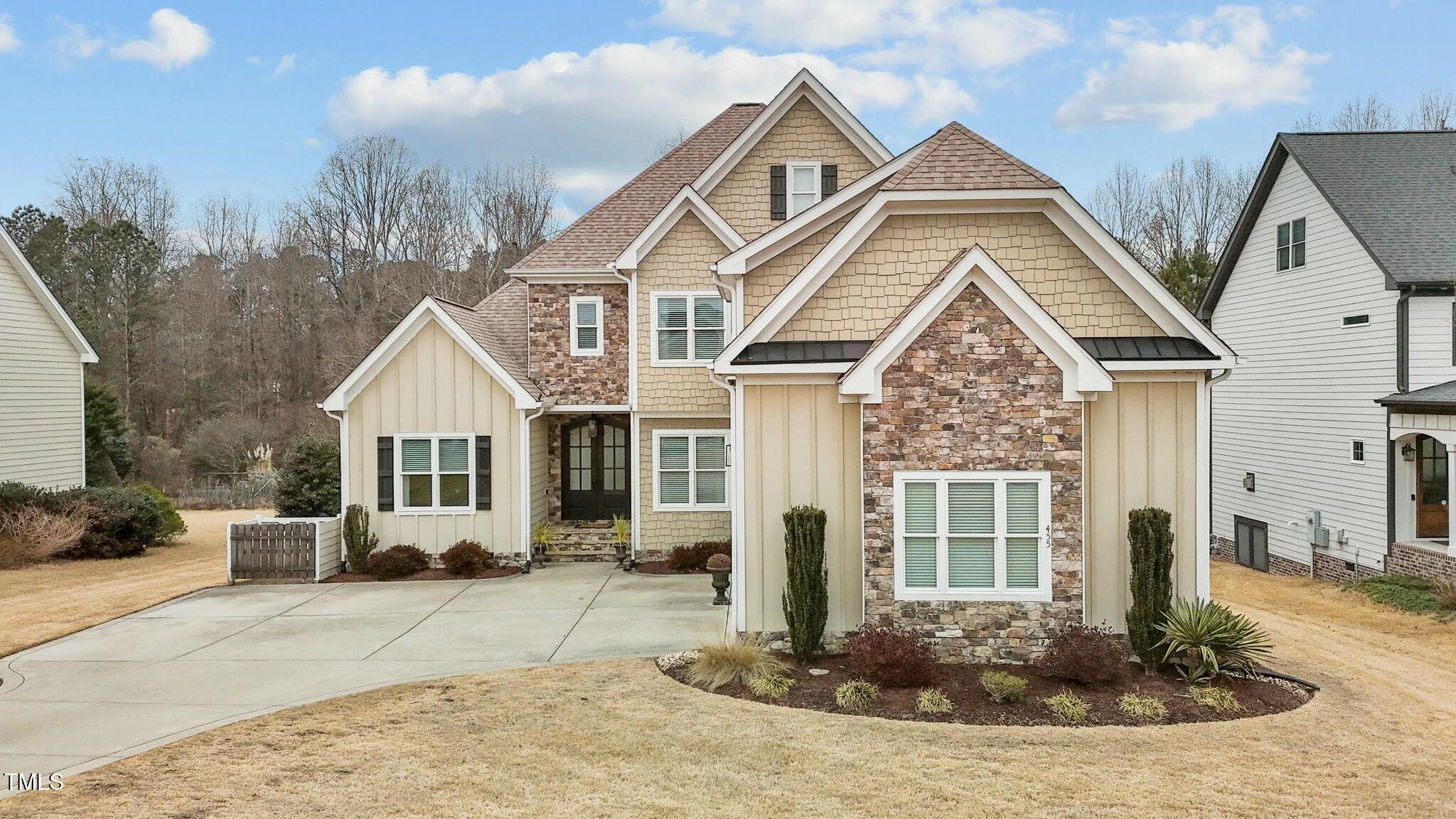 Two-story home with stone accents, beige siding, and a broad concrete driveway.