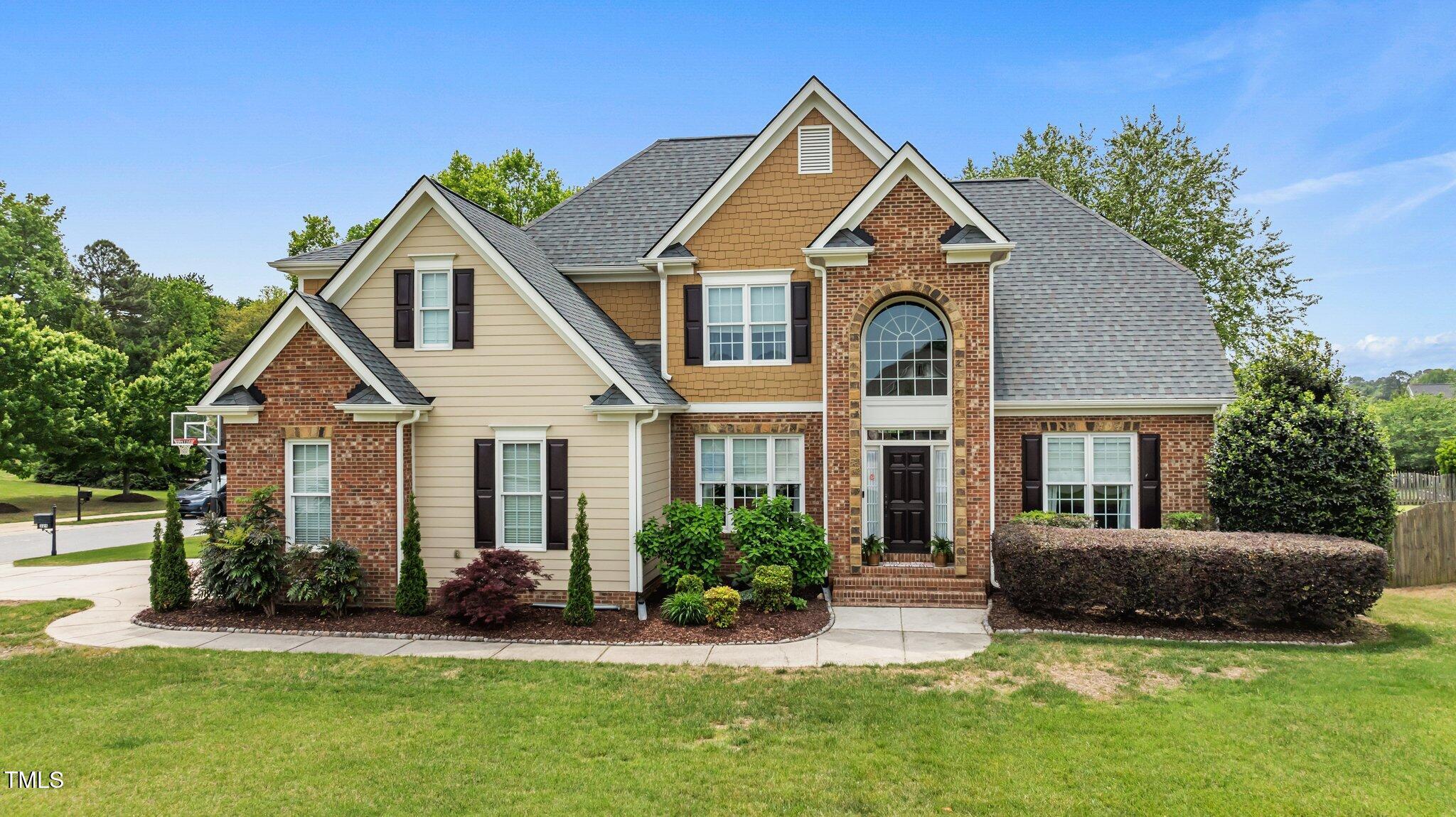 Two-story brick and tan-sided house with multiple gables, an arched entry window, and landscaped front lawn.