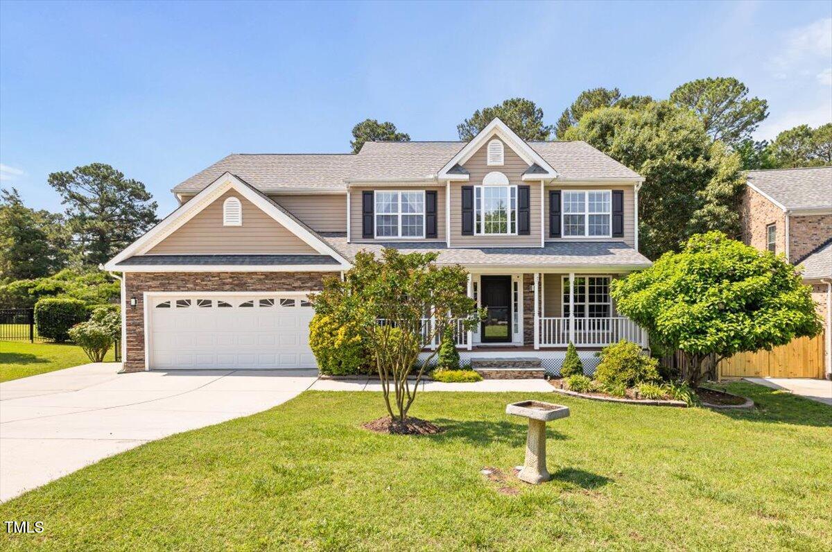 Two-story beige house with a two-car garage, covered porch, and landscaped front lawn.