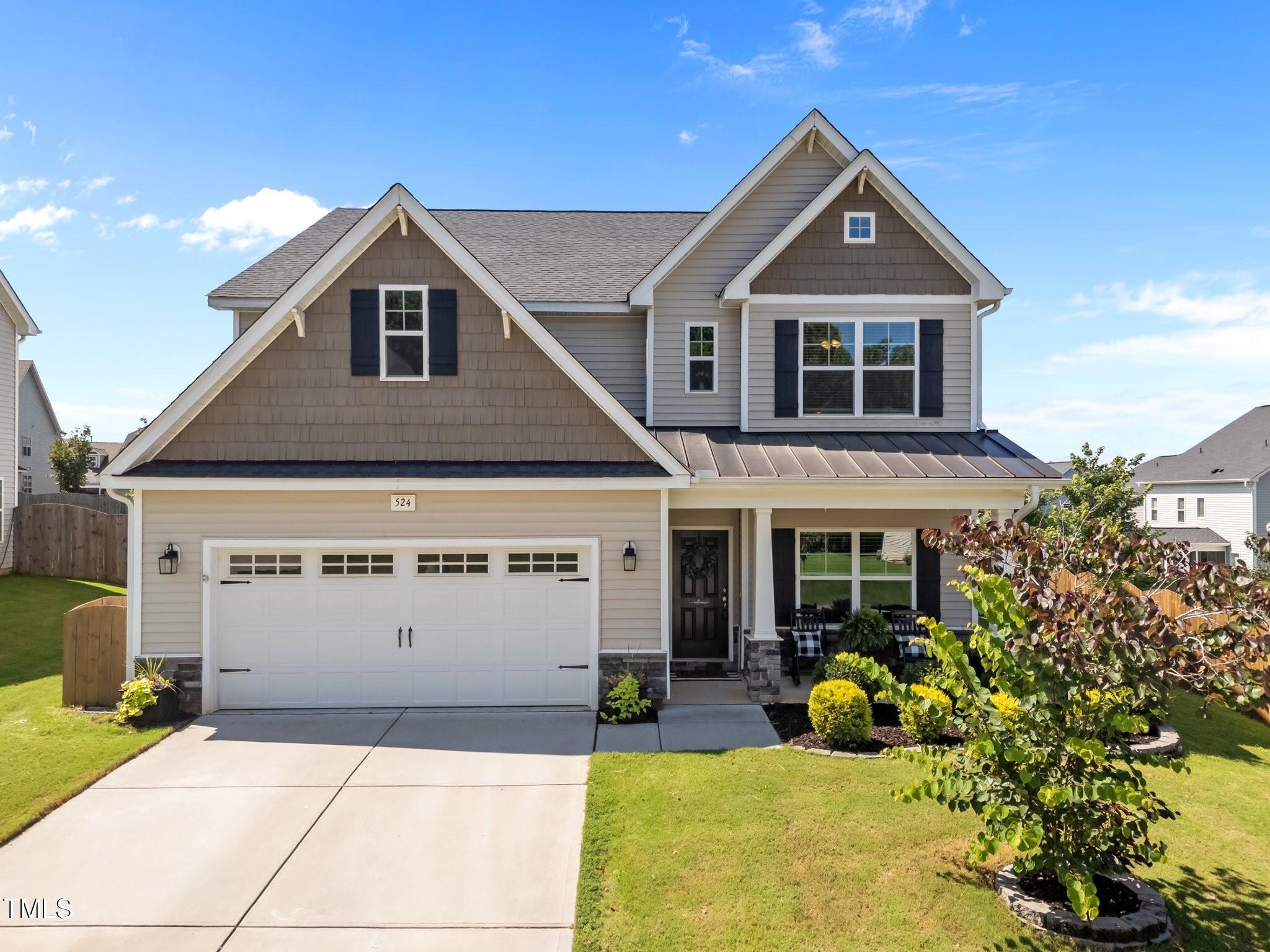 Two-story gray house with front gables, a two-car garage, and landscaped lawn.
