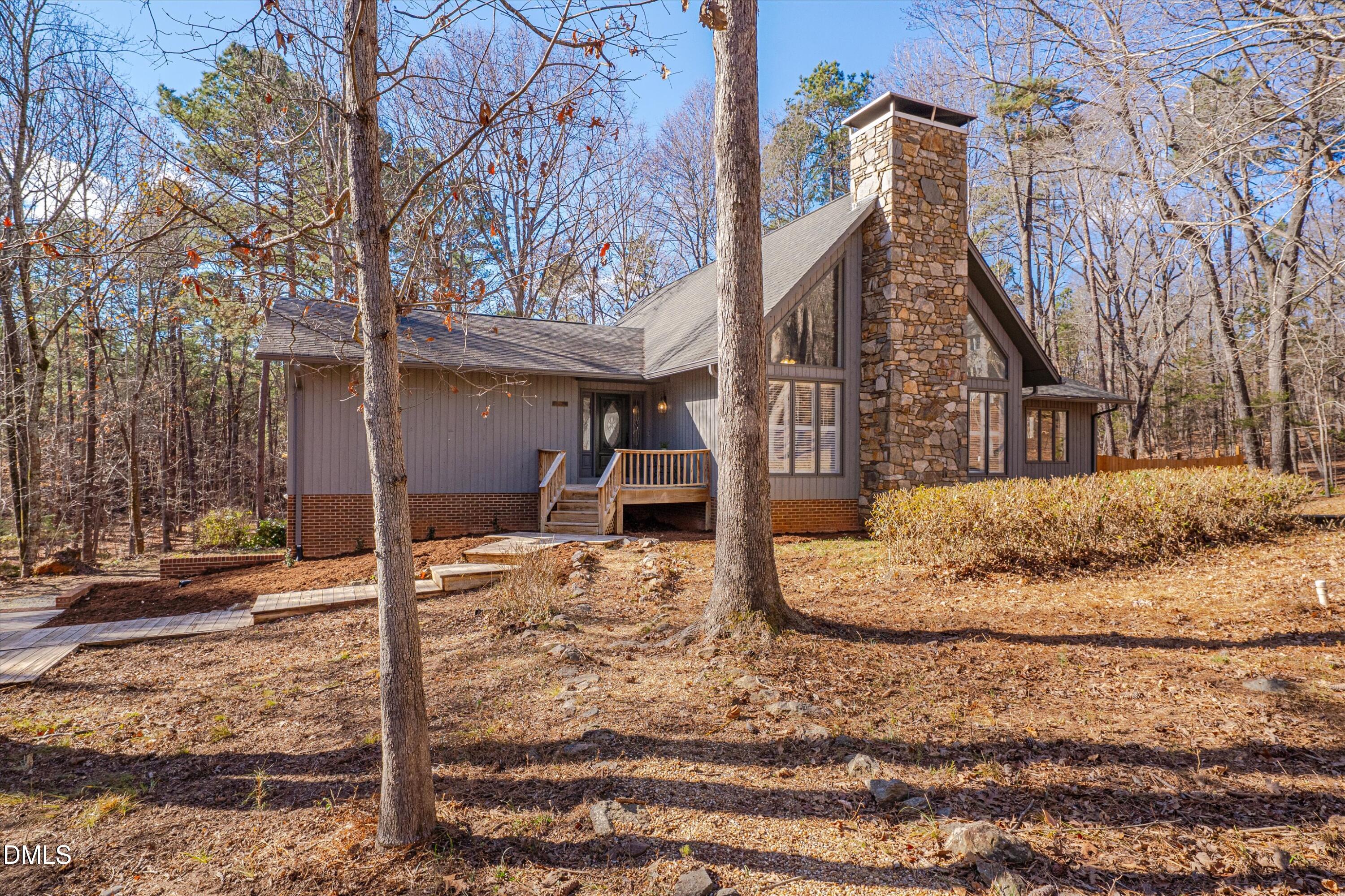 Wooded home with gray siding, a tall stone chimney, and a small wooden entry deck.