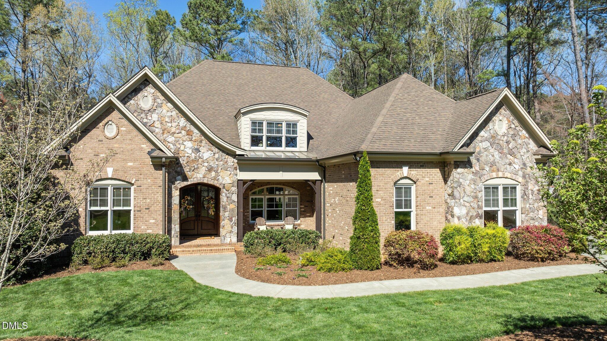 Brick and stone house with a covered entry, landscaped lawn, and wooded backdrop.