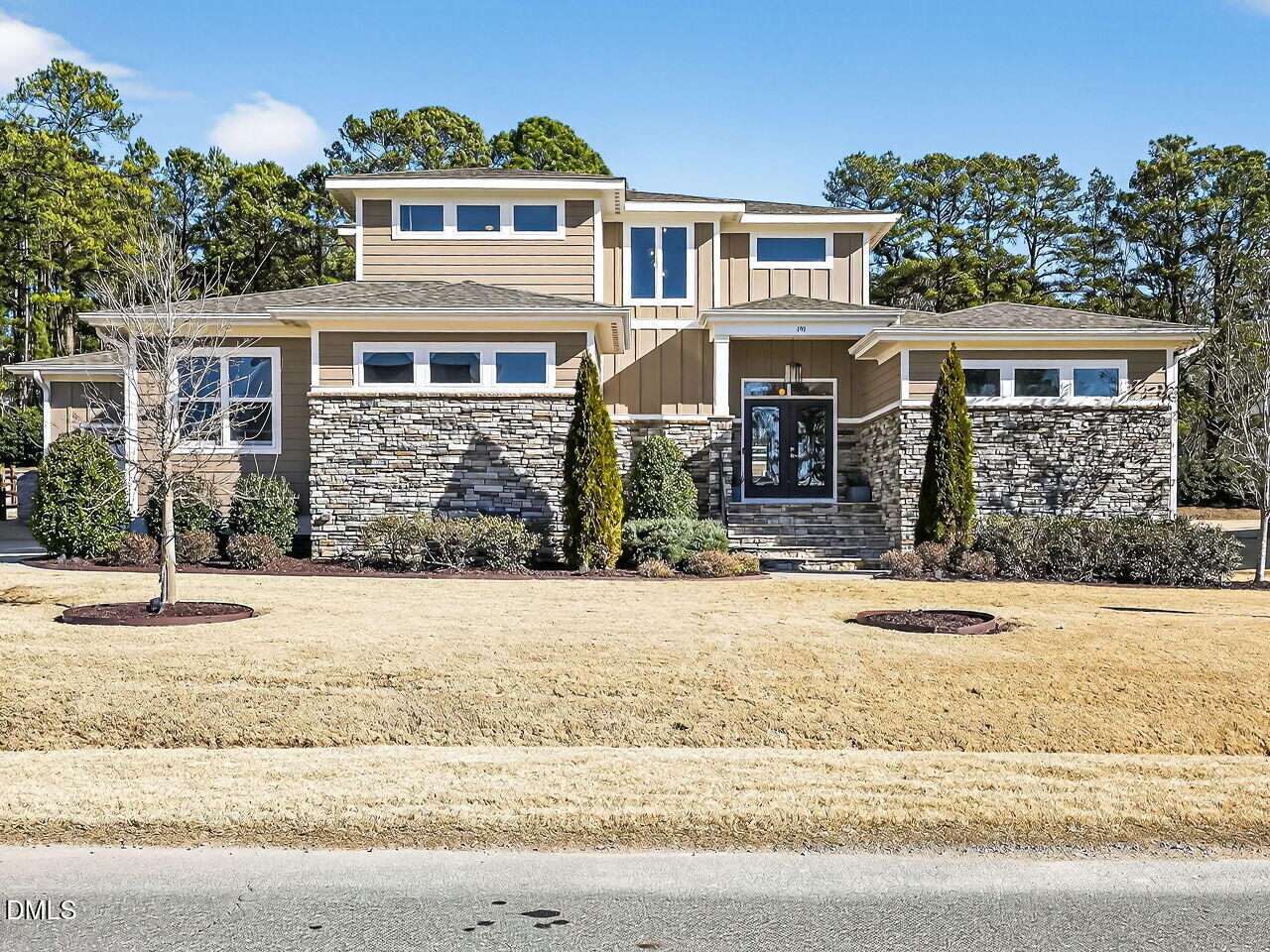 Two-story home with a stone facade, tan siding, and a broad dormant lawn.