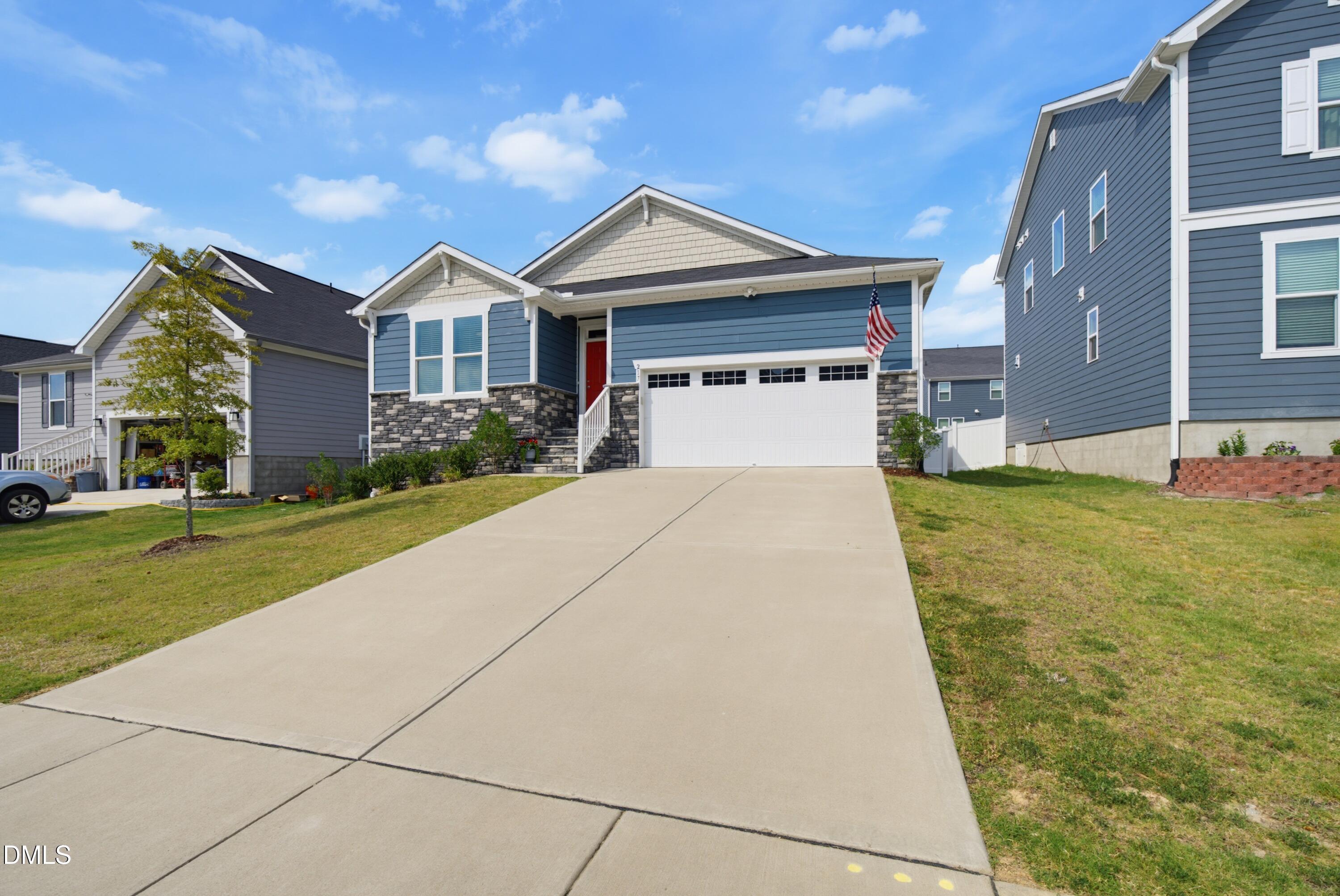 Blue single-story home with stone accents, a red front door, and a broad driveway.