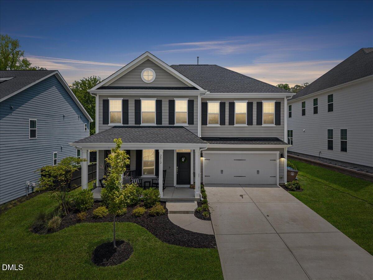 Gray two-story home with black shutters, a covered porch, and an attached double garage at dusk.