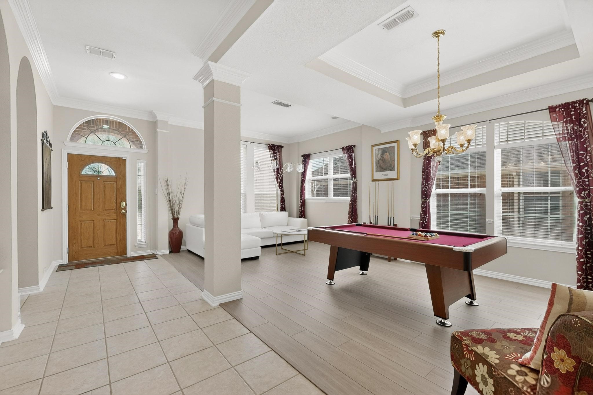 Open entry and living area with a pool table, white sectional, and large curtained windows.