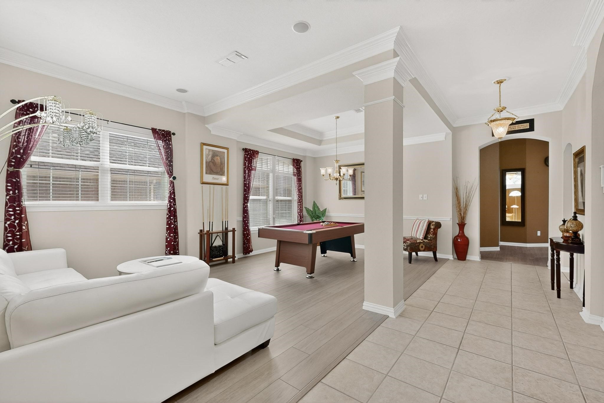 Open-plan living room with a pool table, white sectional, and burgundy curtains.
