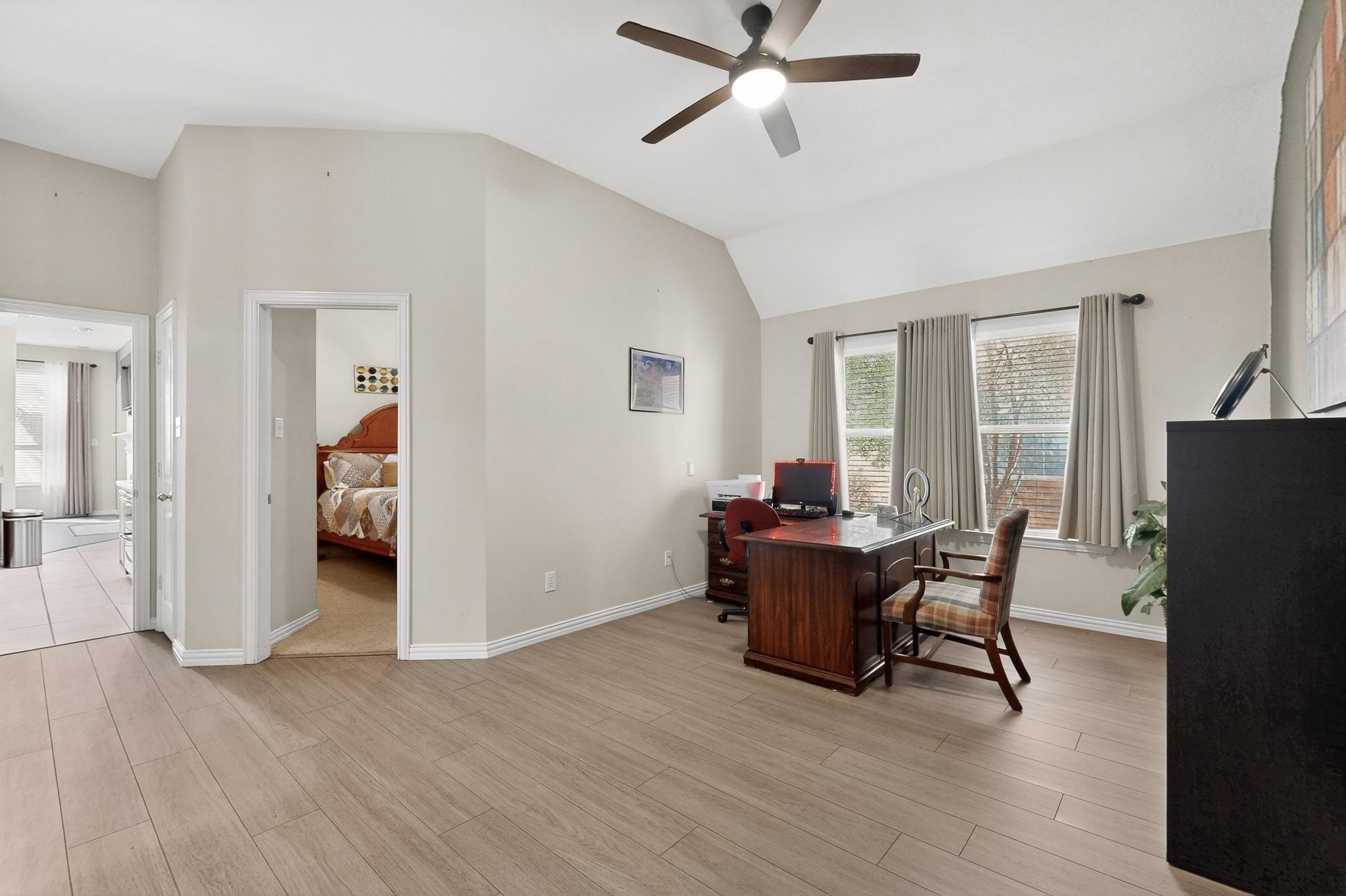 Home office with a high sloped ceiling, wood-look floors, and a desk beside curtained windows.