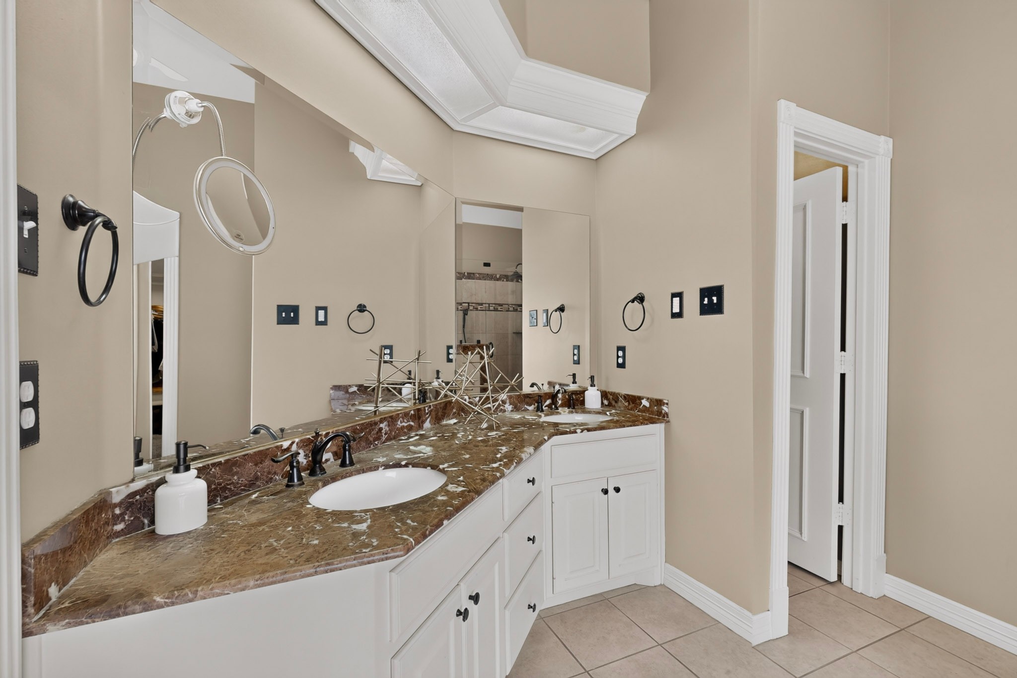 Bathroom with a long brown marble vanity, white cabinets, dark faucets, and a large mirror.