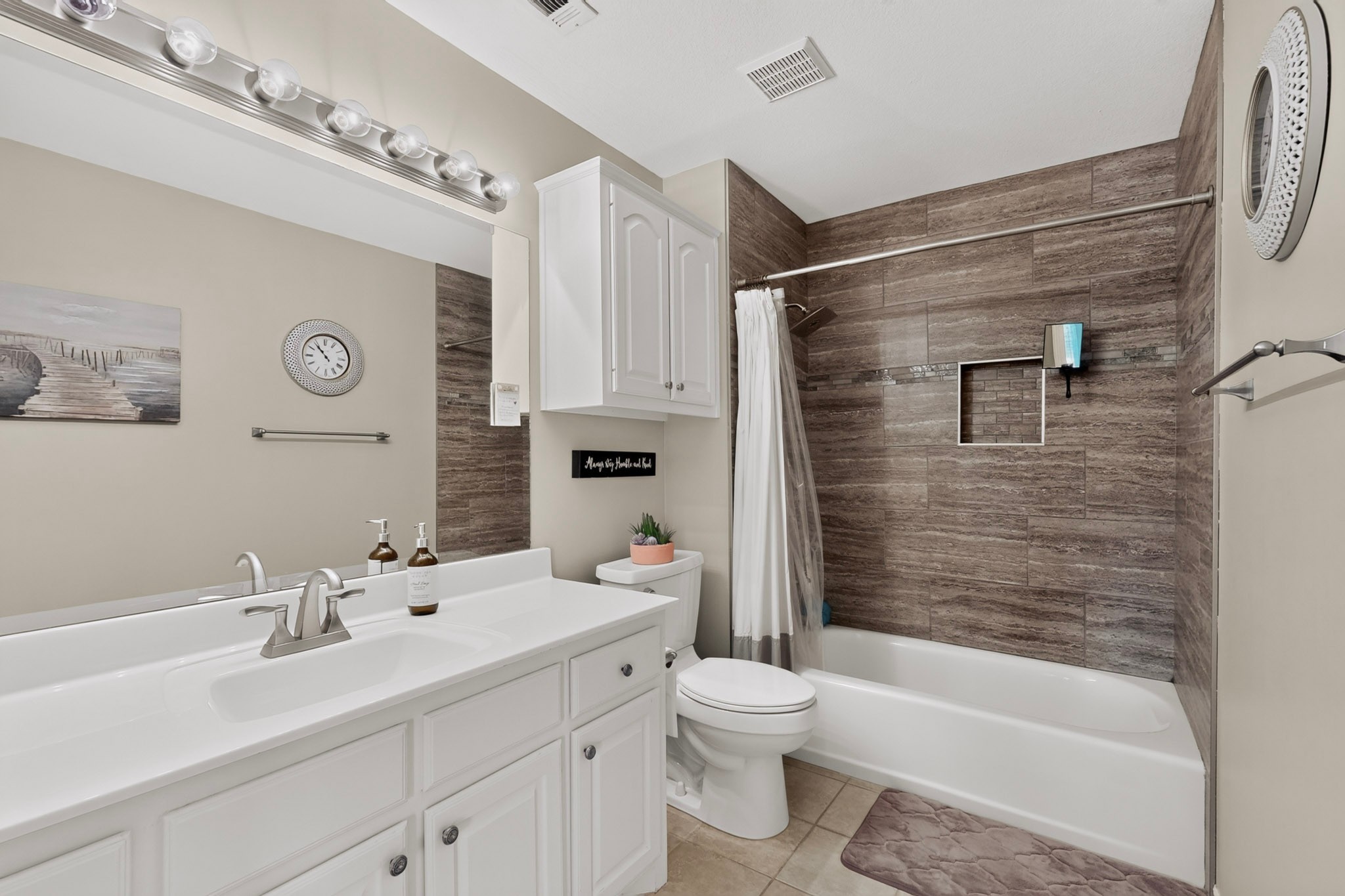 Bathroom with a white vanity and bathtub surrounded by brown stone-look tile.