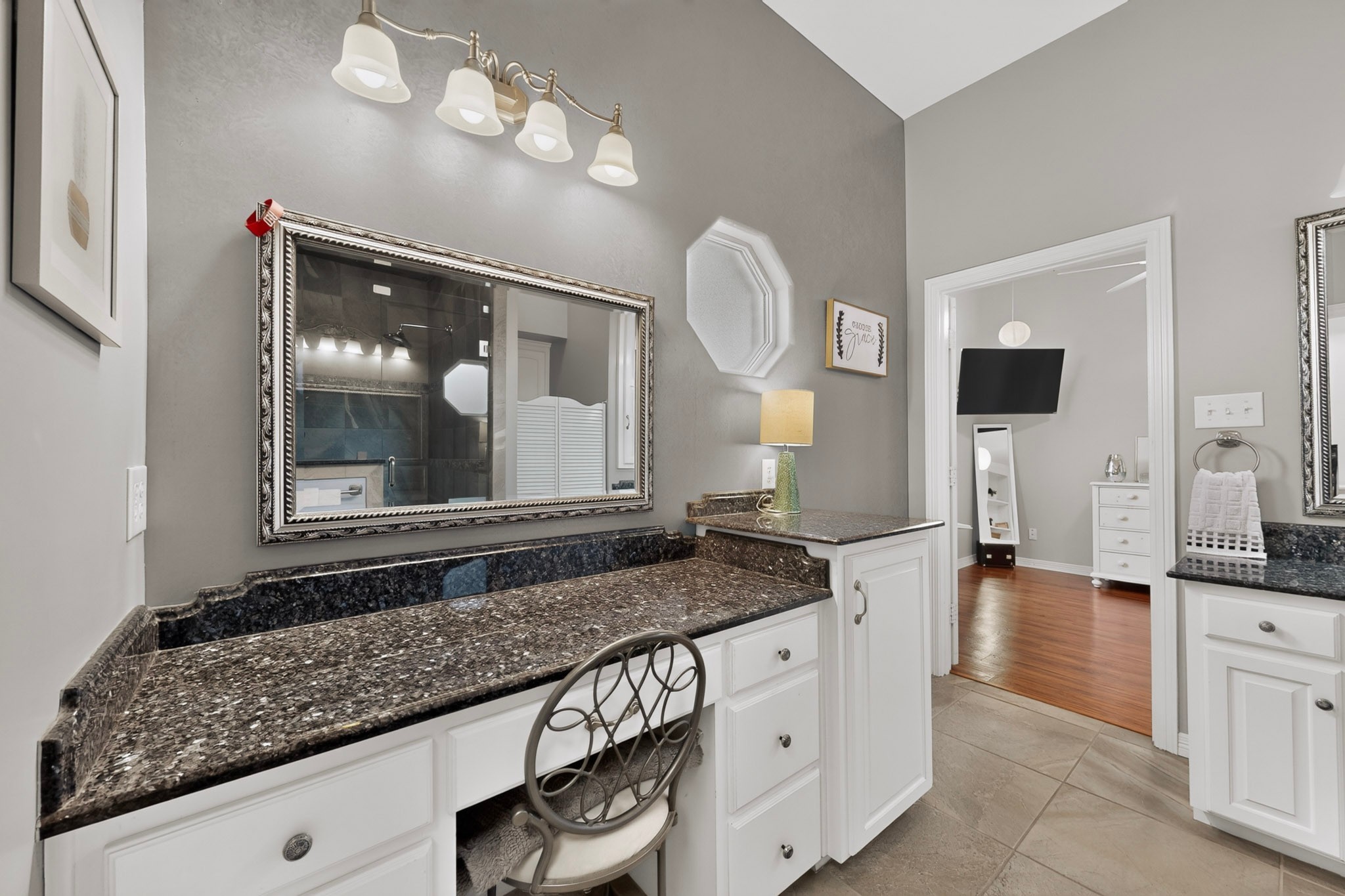 Bathroom vanity with dark granite counters, white cabinetry, an ornate mirror, and a makeup stool.