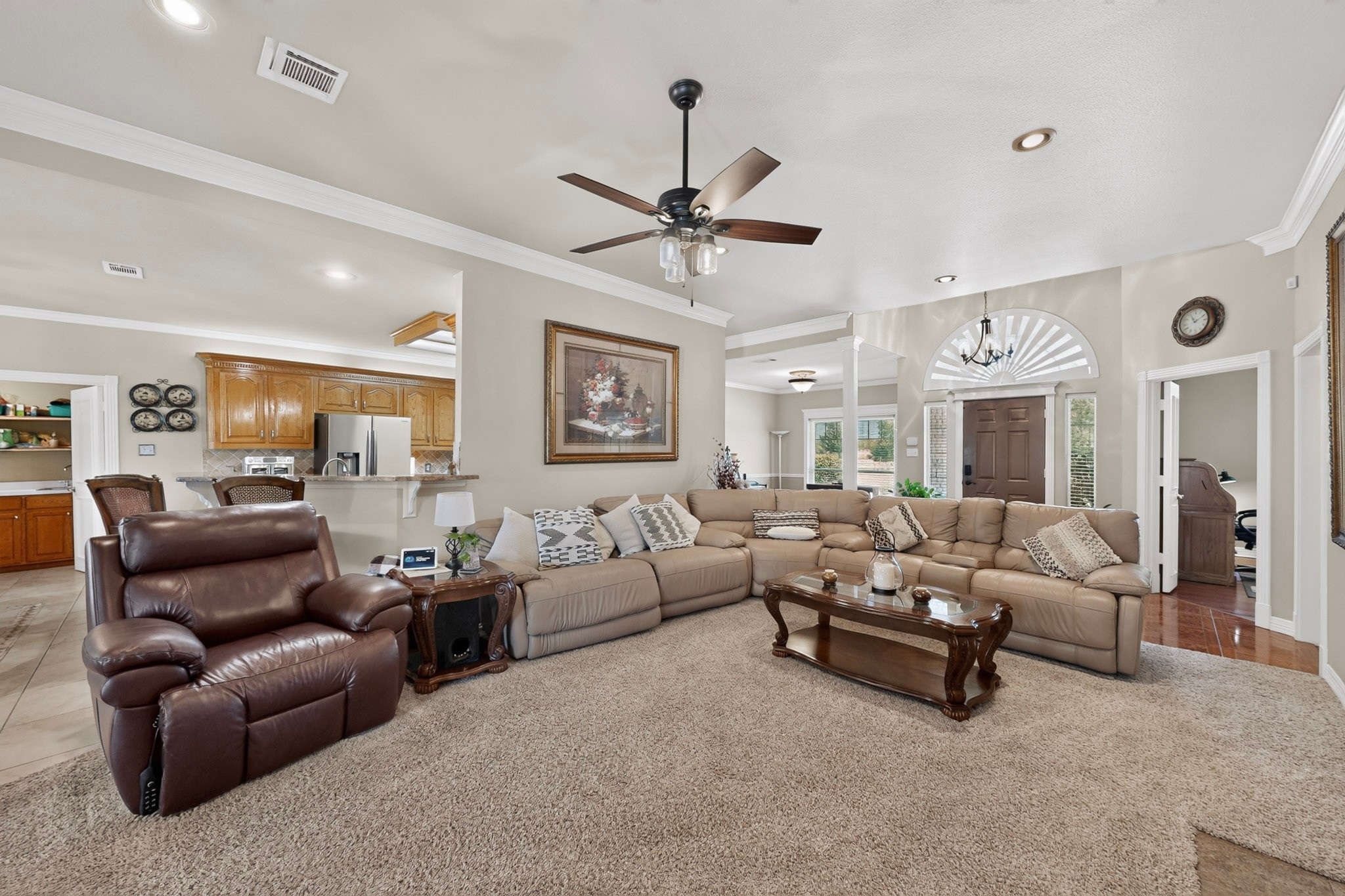 Furnished living room with a beige sectional, leather recliner, and arched window over the front door.