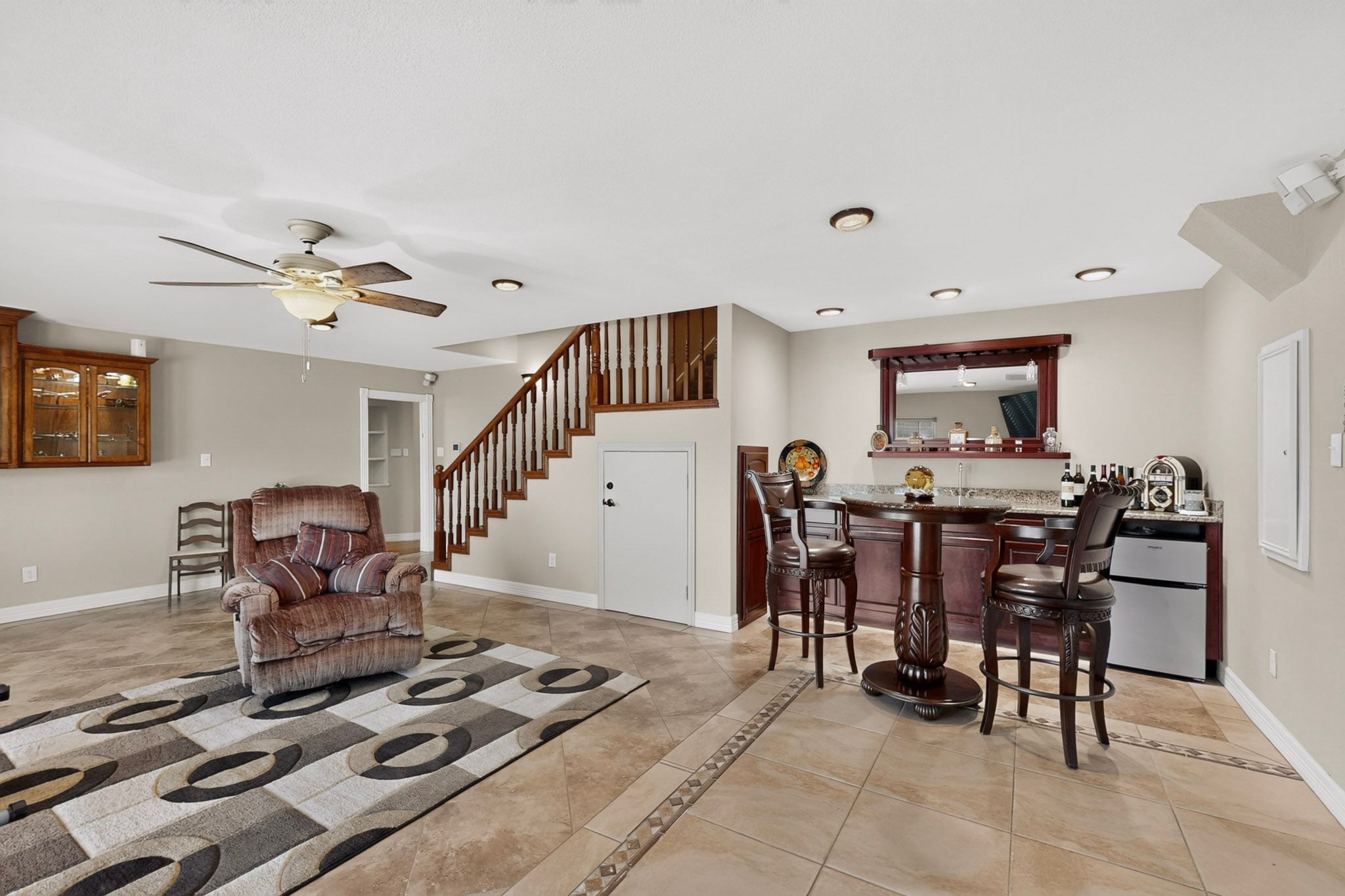 Furnished living area with a dark wood bar, staircase, recliner, and patterned rug.