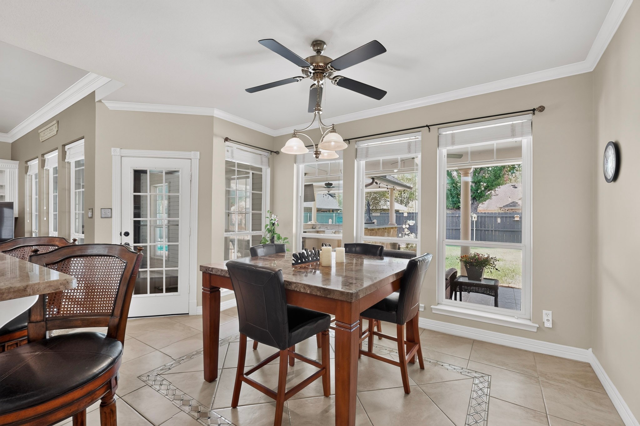Dining area with a stone-topped table, dark chairs, and large windows overlooking a fenced yard.