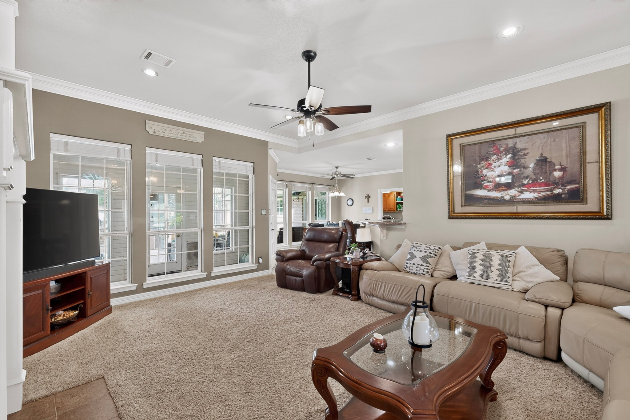 Furnished living room with a tan sectional, leather recliner, tall windows, and beige carpeting.