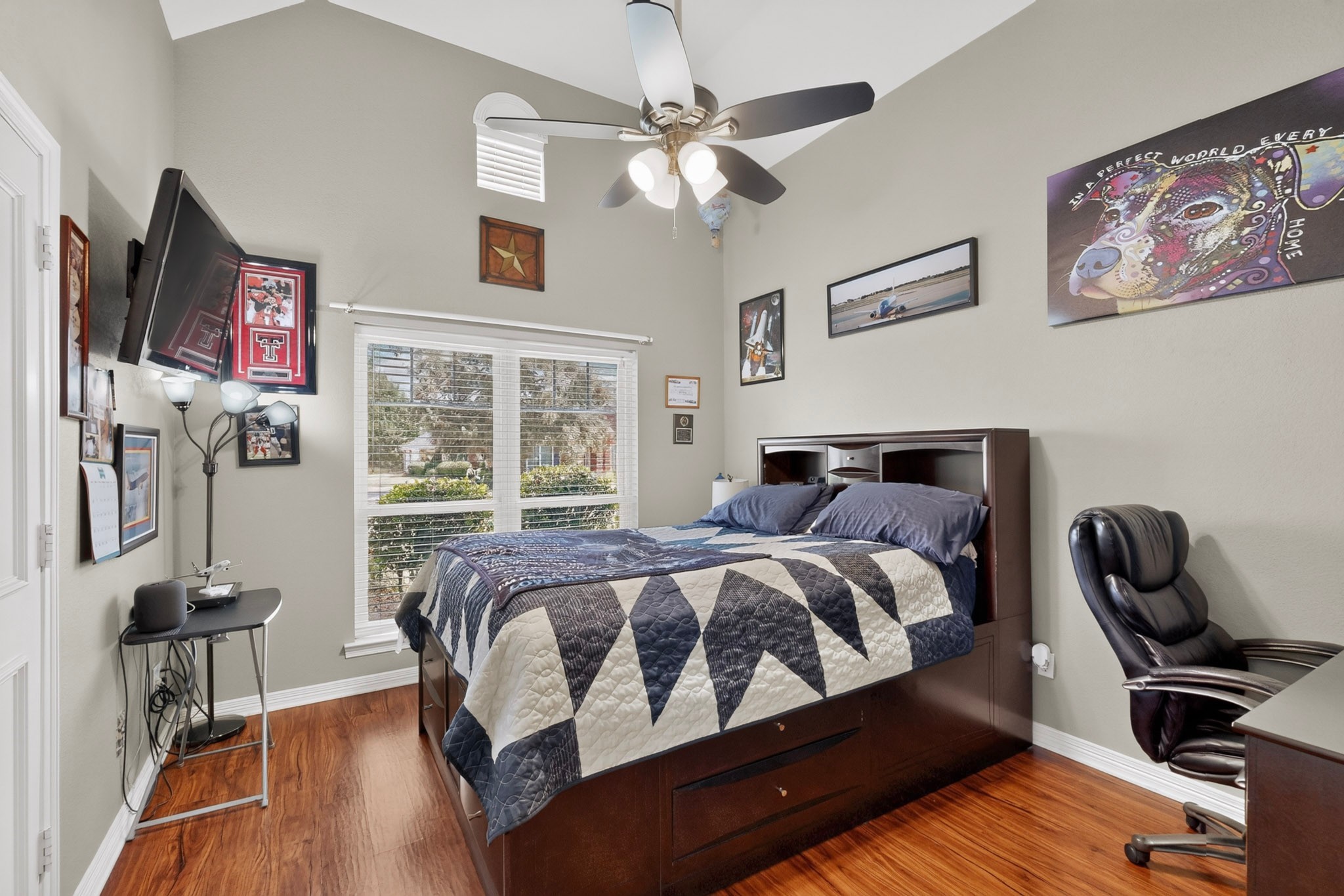 Bedroom with a dark wood storage bed, geometric quilt, hardwood floors, and framed sports memorabilia.