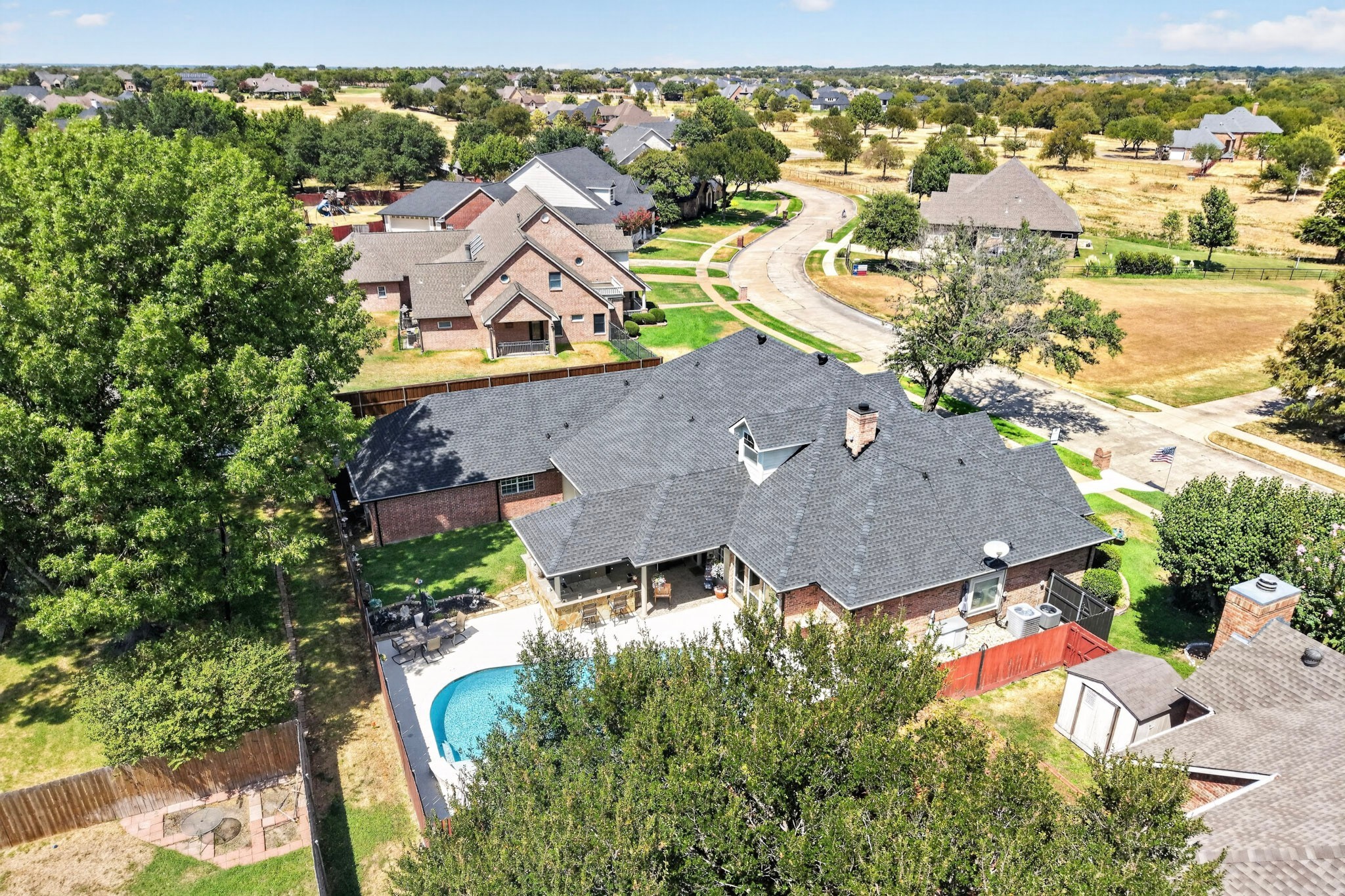 Aerial view of a brick house with a fenced backyard, curved pool, and patio.