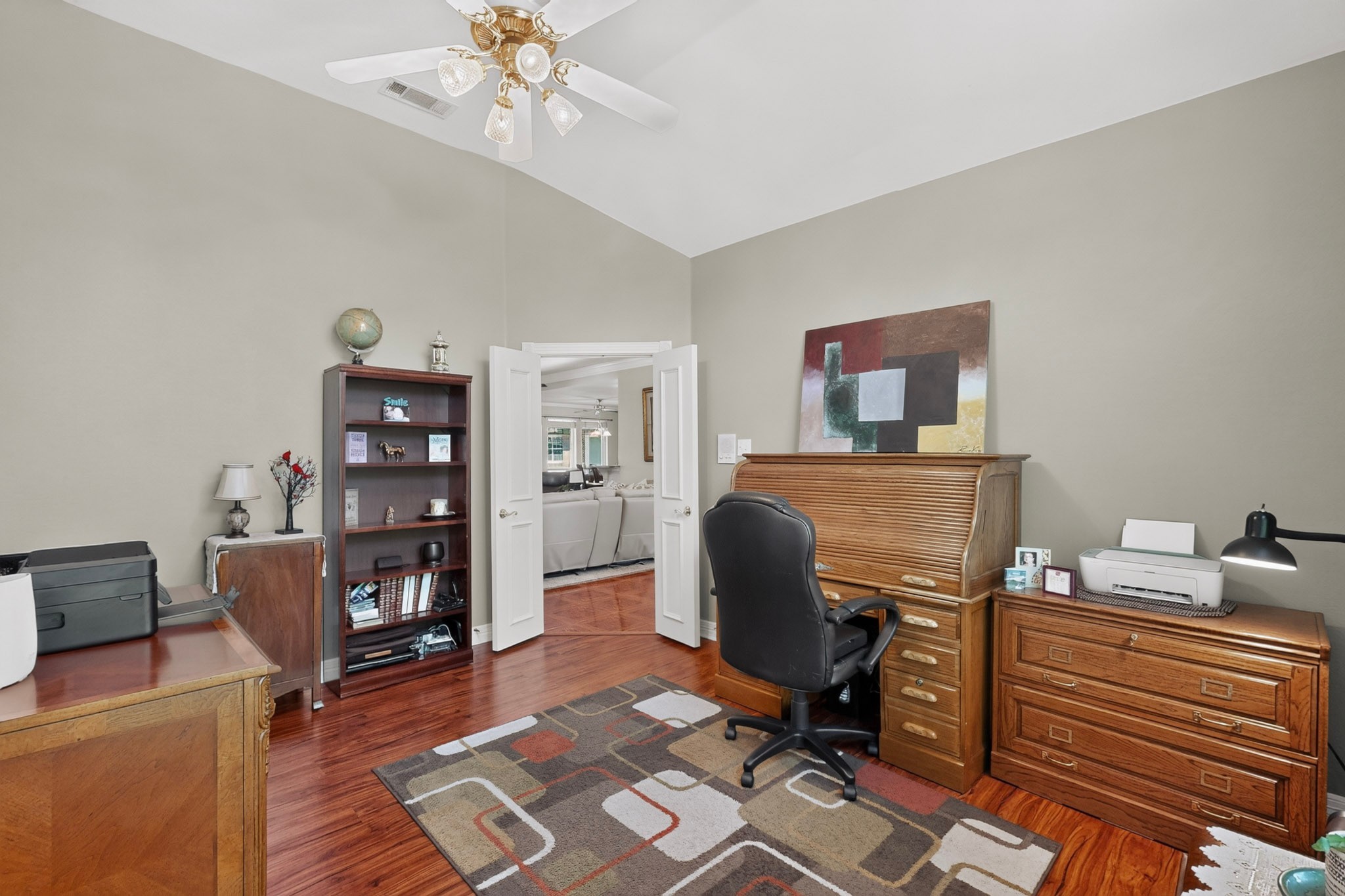Furnished home office with hardwood floors, wooden desks, a bookcase, and a vaulted ceiling.