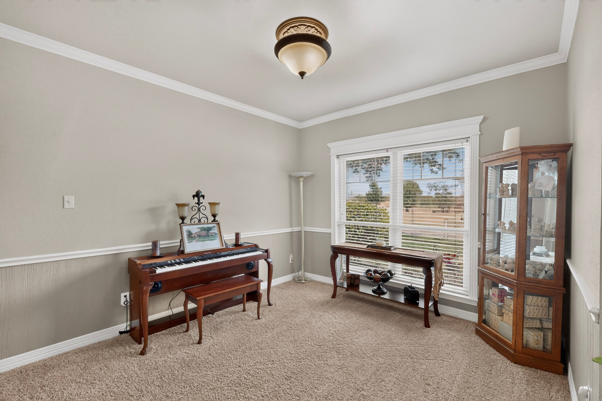 Furnished room with a wooden keyboard, glass-front display cabinet, and wide window with blinds.