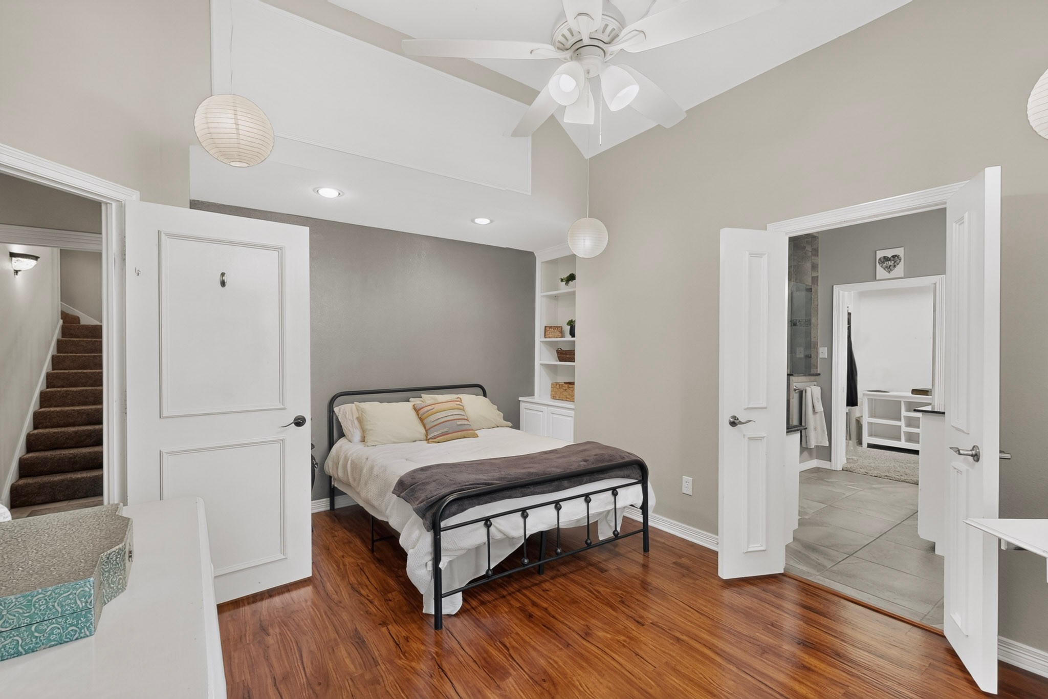 Bedroom with a black metal bed, vaulted ceiling, and open doors to an adjoining bathroom.