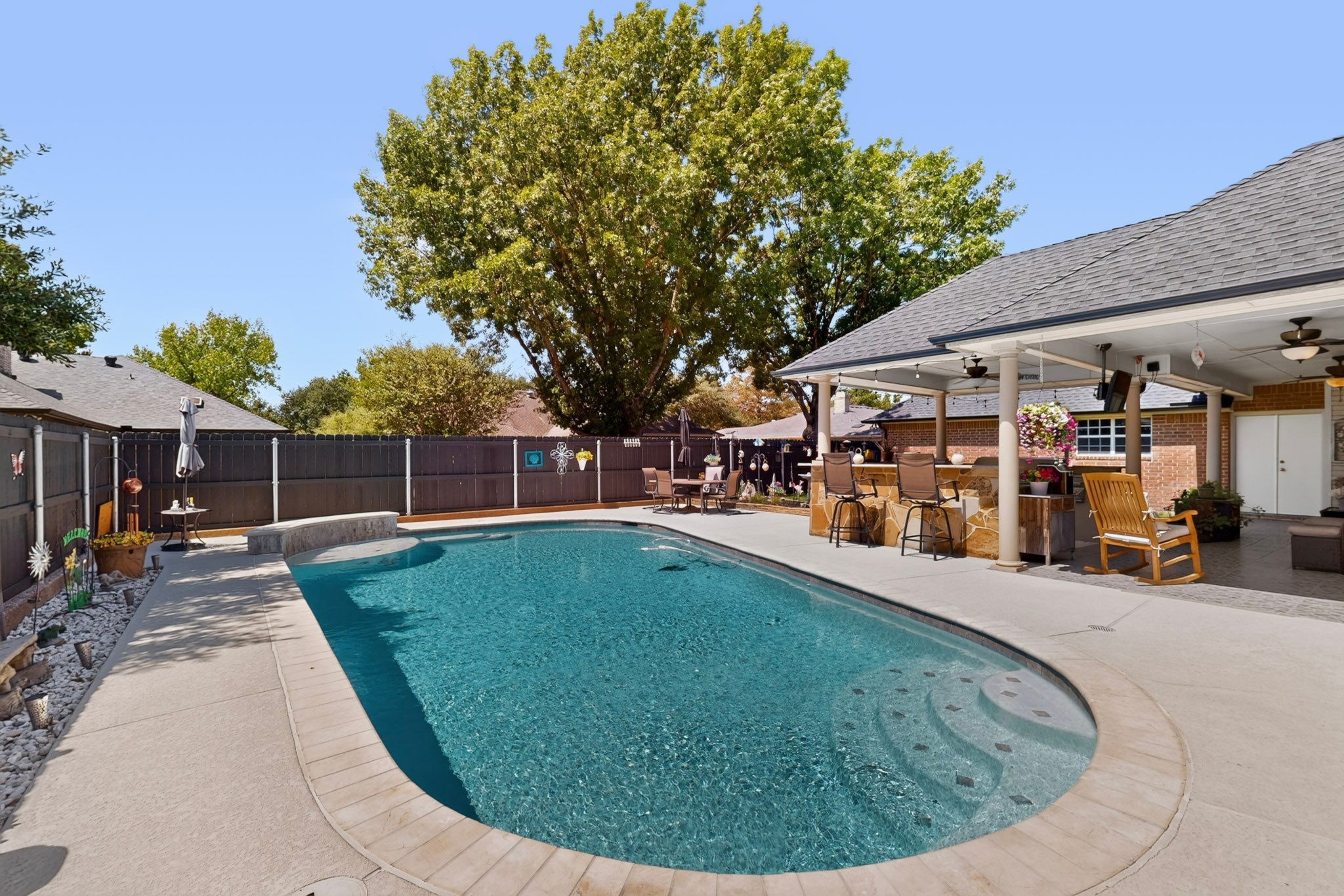 Backyard swimming pool with a shallow lounging area and a covered patio with bar seating.