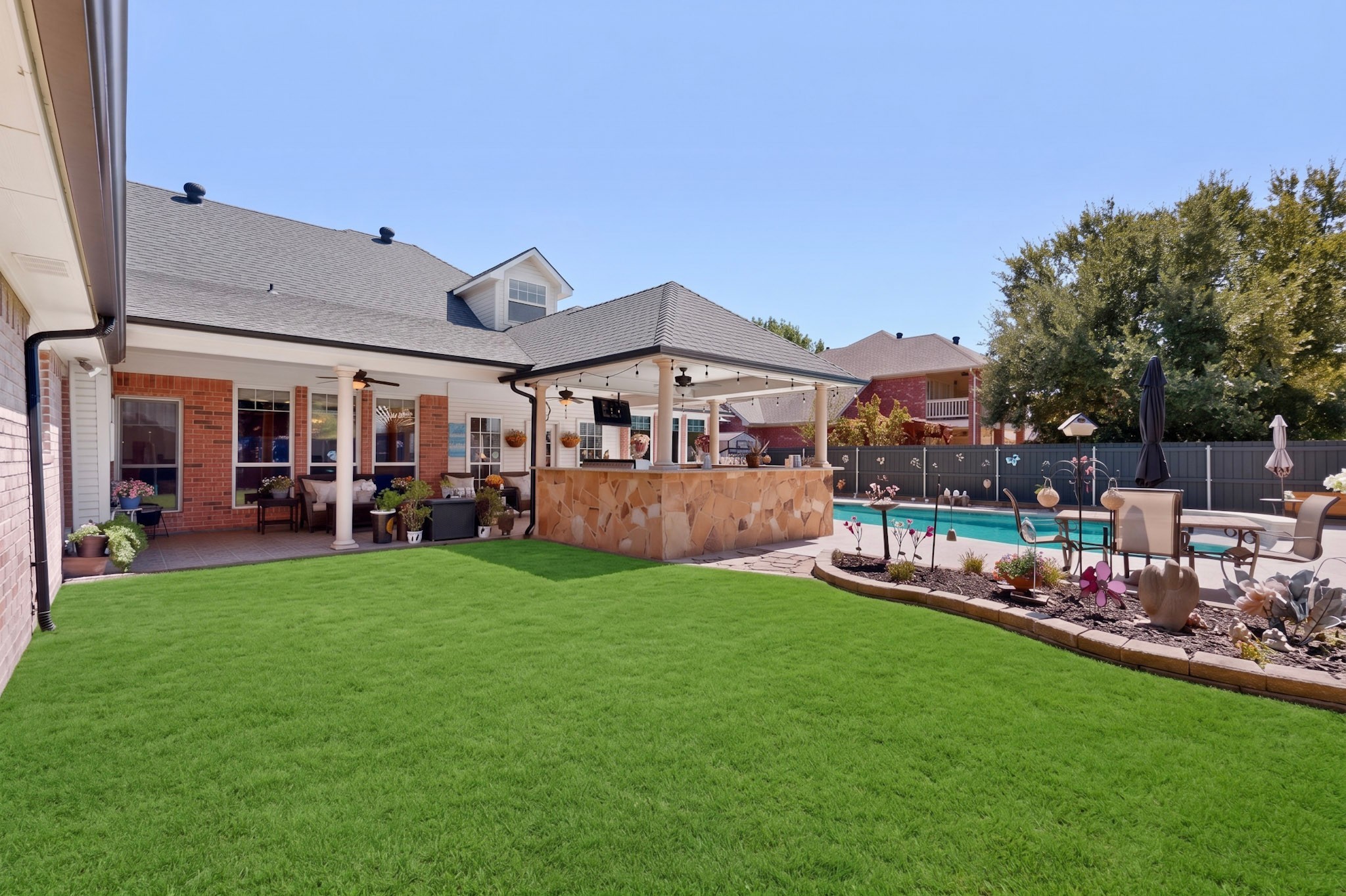 Backyard with a swimming pool, covered patio and stone outdoor bar, landscaped beds, and a broad lawn.
