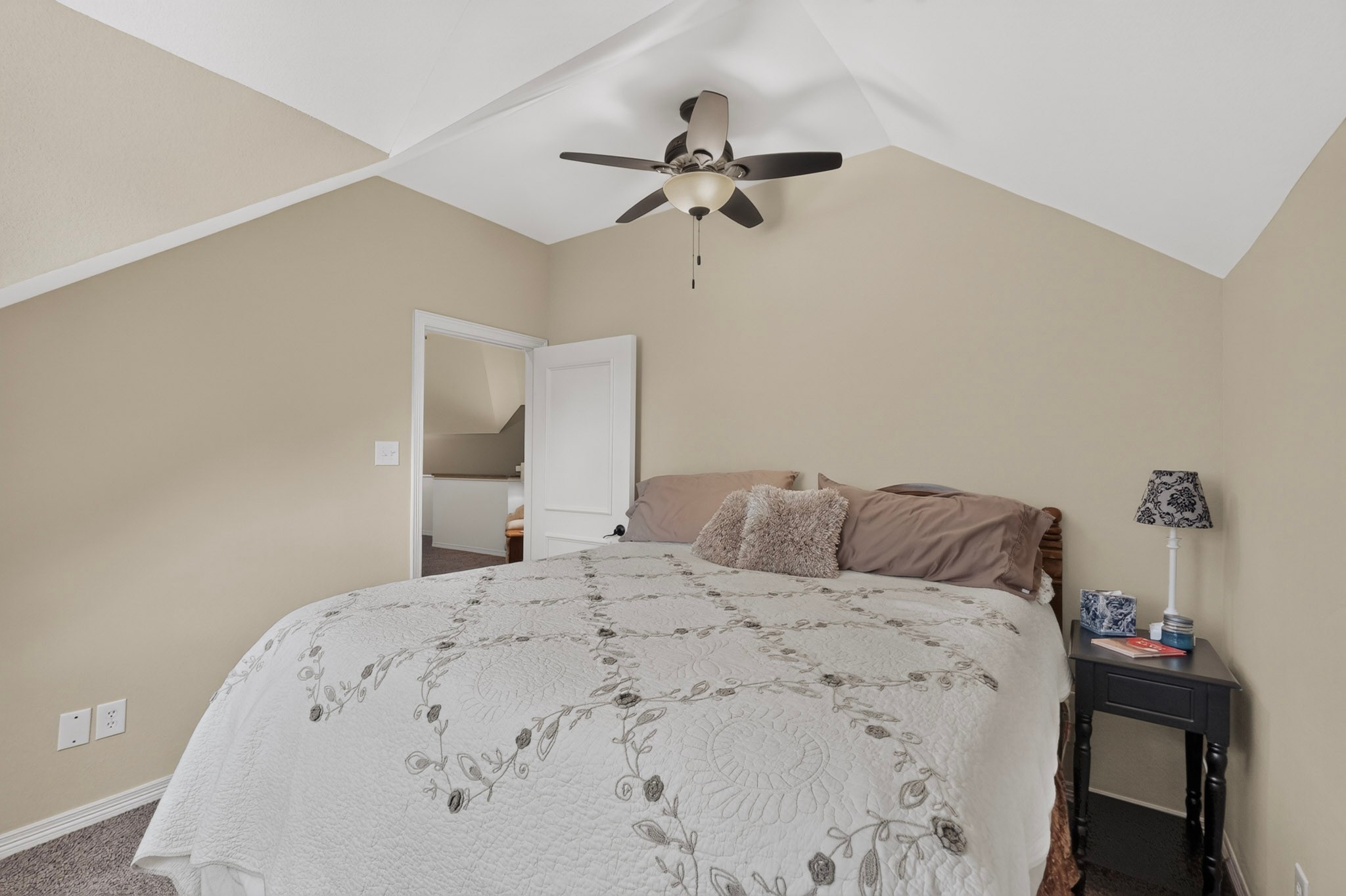 Furnished bedroom with a large bed beneath a vaulted ceiling and ceiling fan.