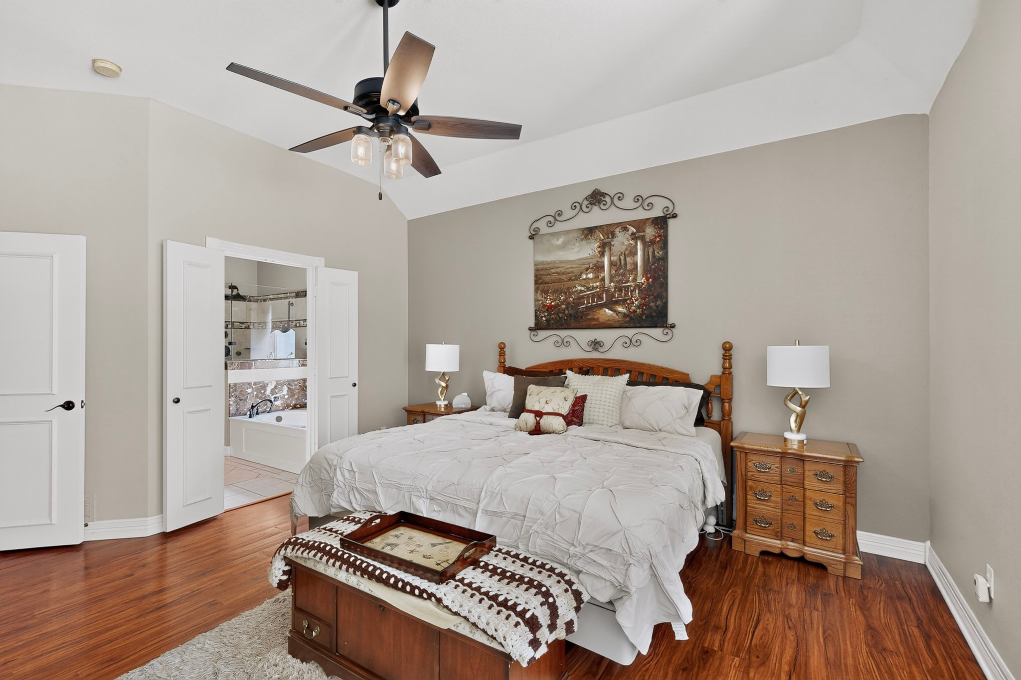 Bedroom with a wooden four-poster bed, hardwood floors, and an open doorway to a tiled bathroom.