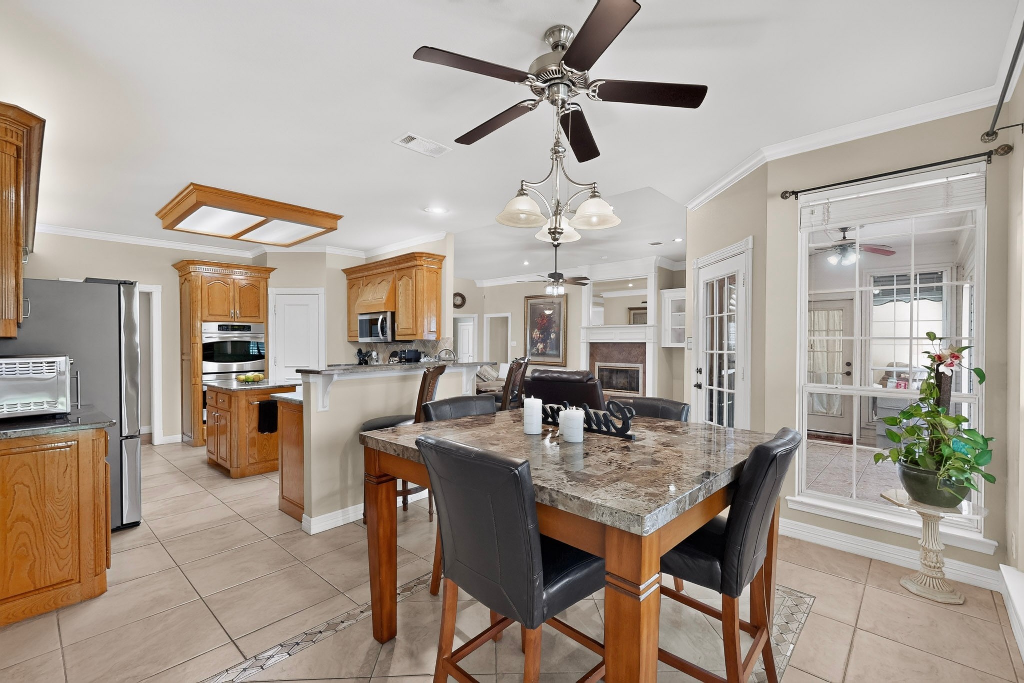 Open kitchen and dining area with wood cabinetry, a granite-topped table, and a living room fireplace beyond.