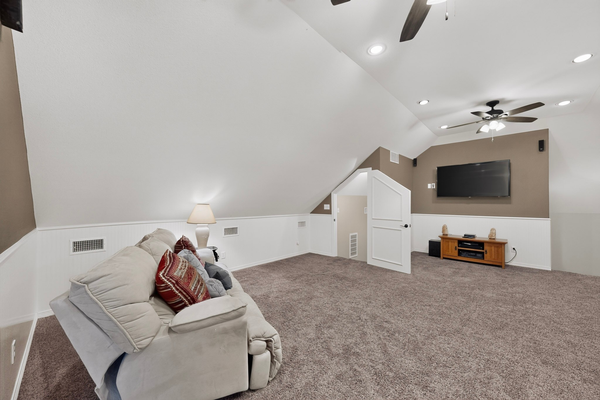 Upstairs living room with a sloped ceiling, white sofa, brown carpet, and wall-mounted television.