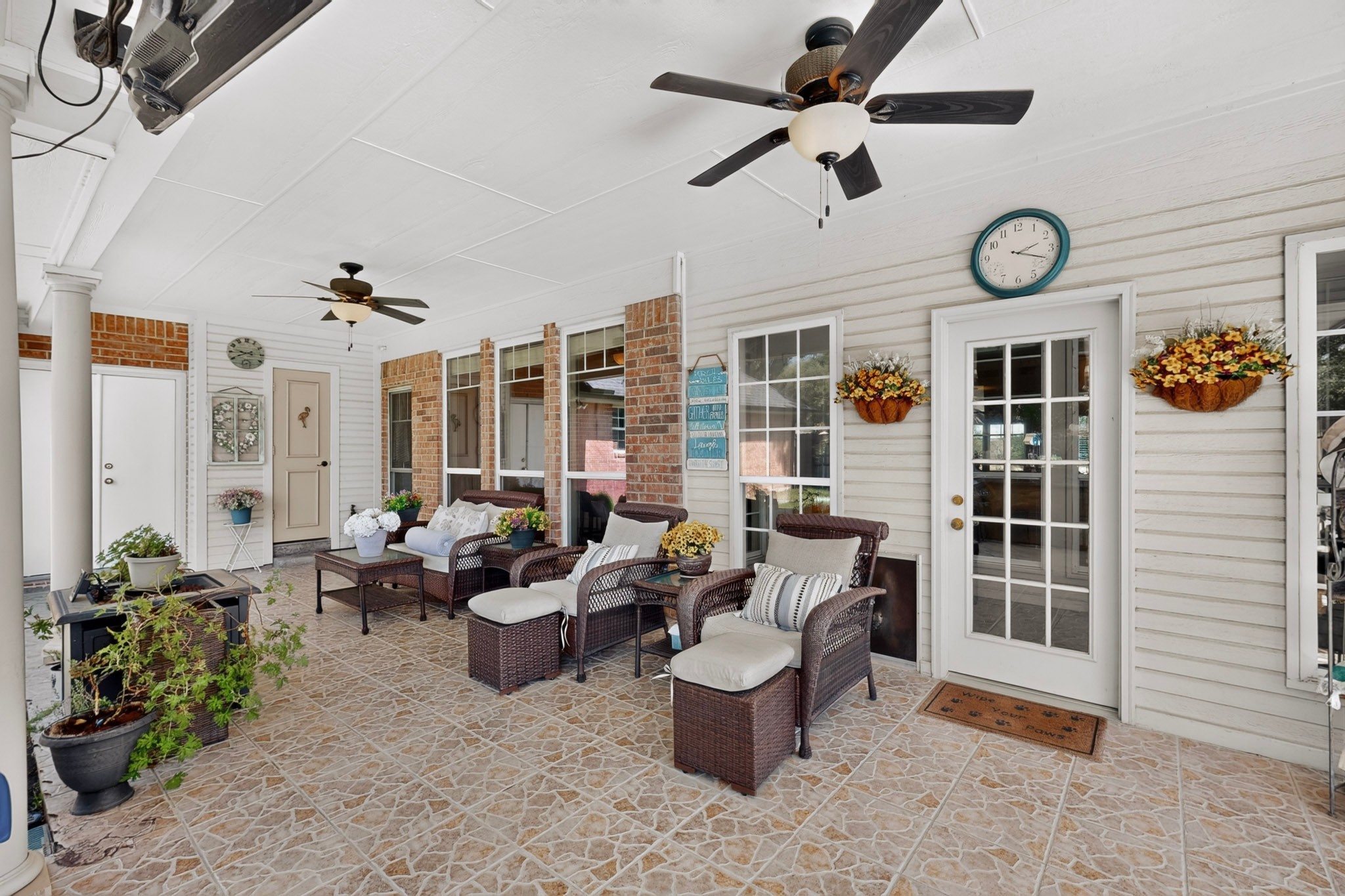 Covered patio with wicker seating, patterned tile flooring, brick accents, and flower baskets.
