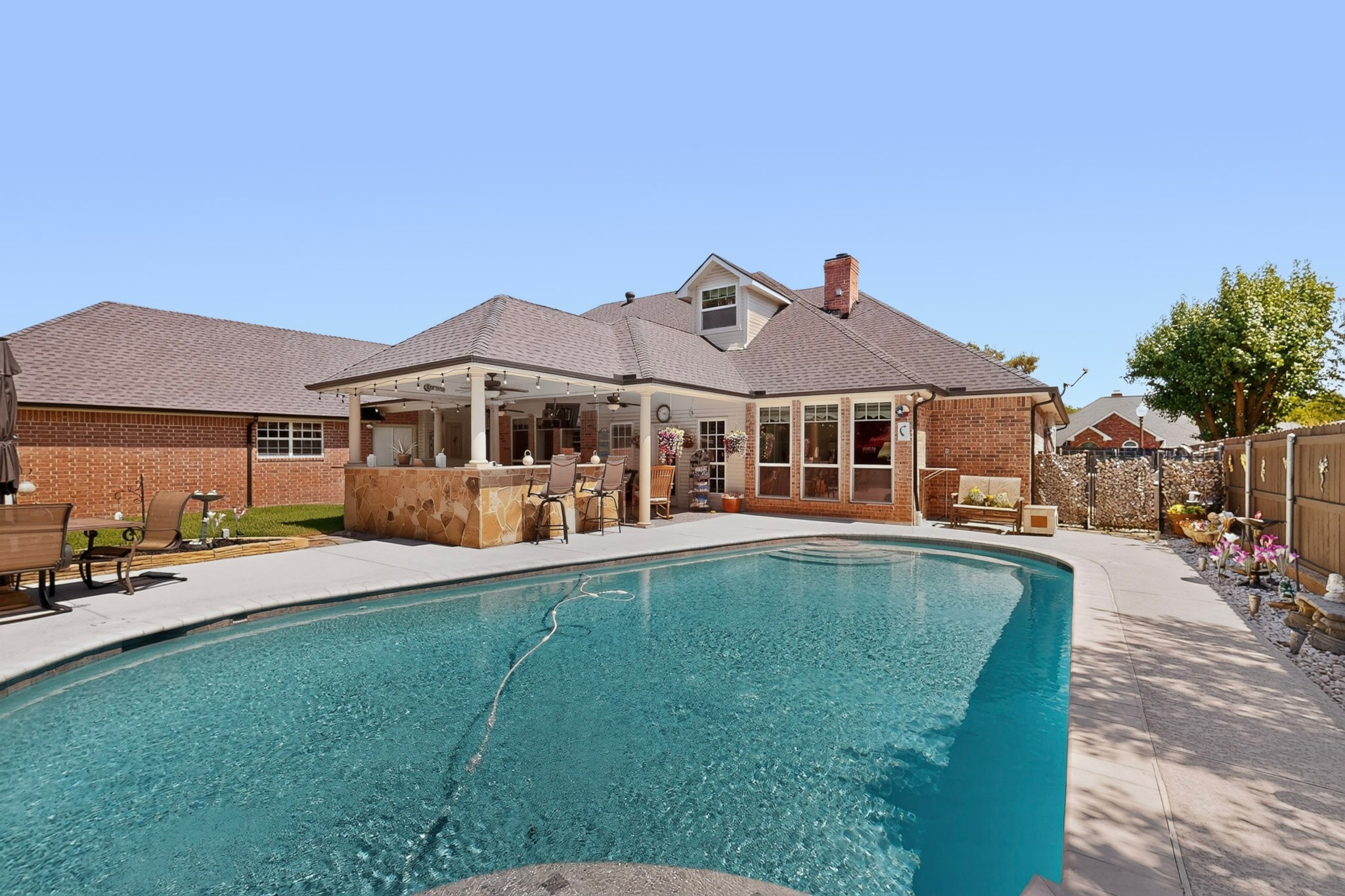 Brick home behind a large swimming pool, with a covered patio and stone bar.