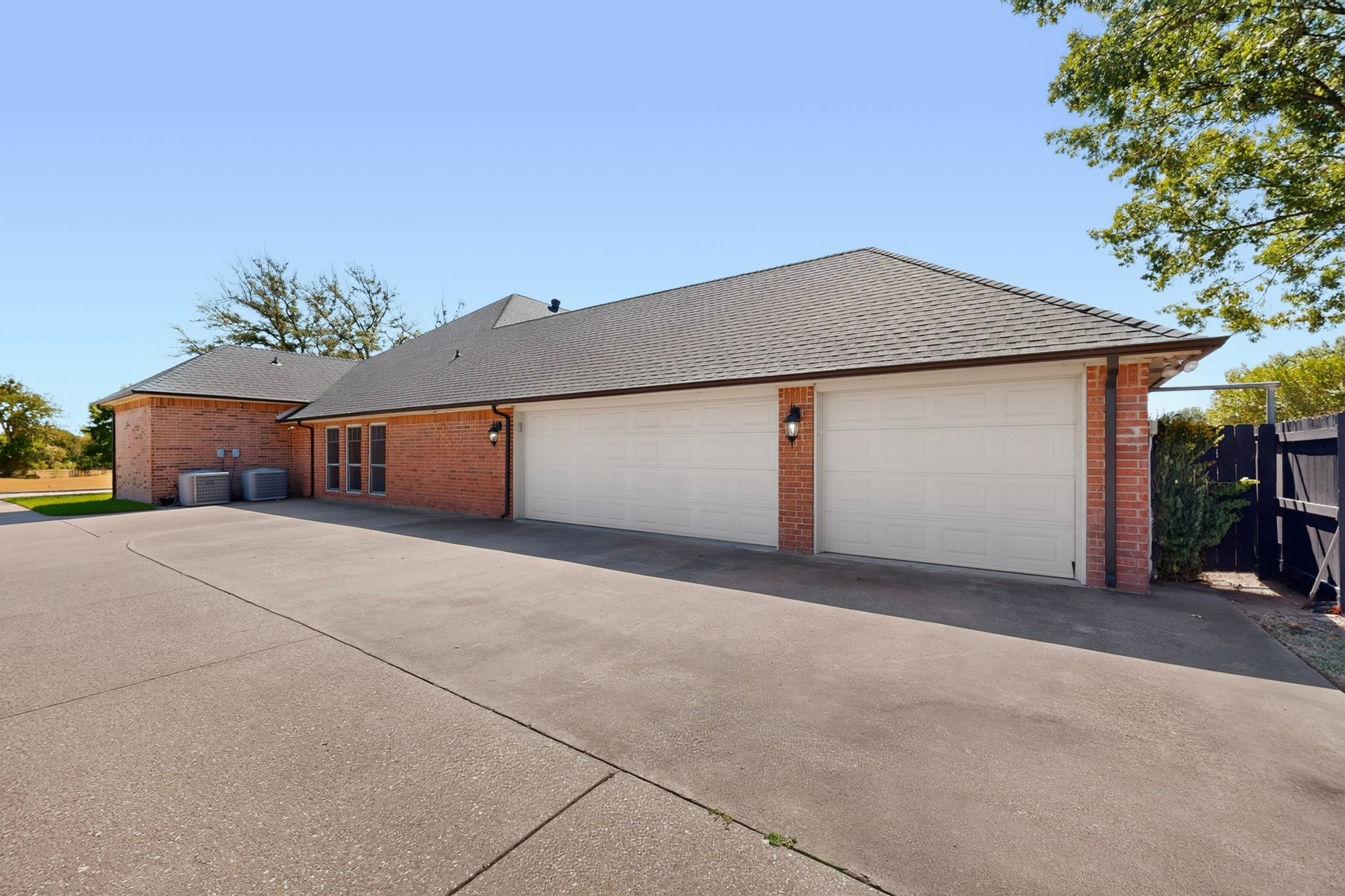 Red-brick home with two white garage doors and a wide concrete driveway.