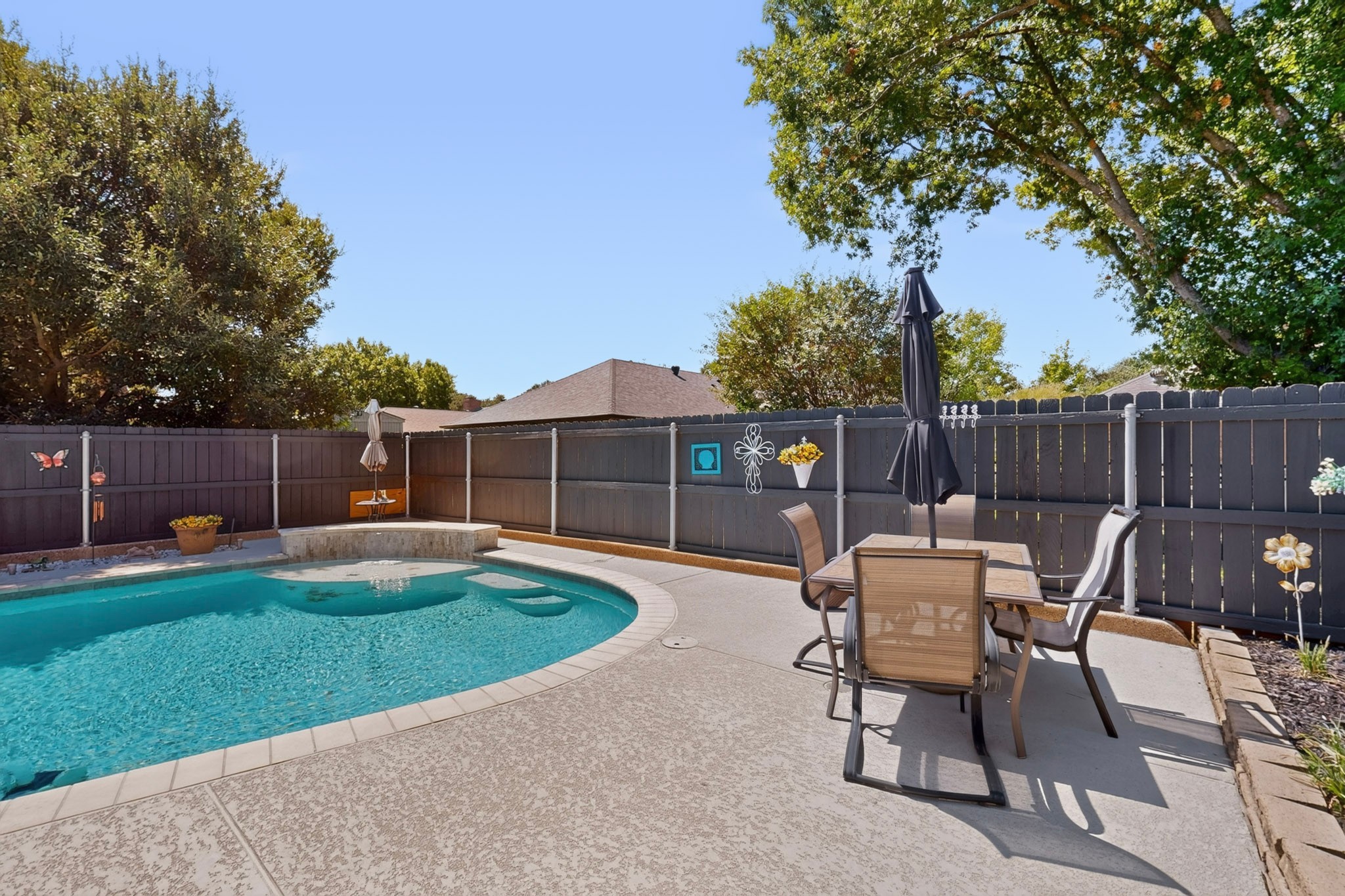 Backyard swimming pool beside a fenced patio with outdoor dining furniture and a closed umbrella.
