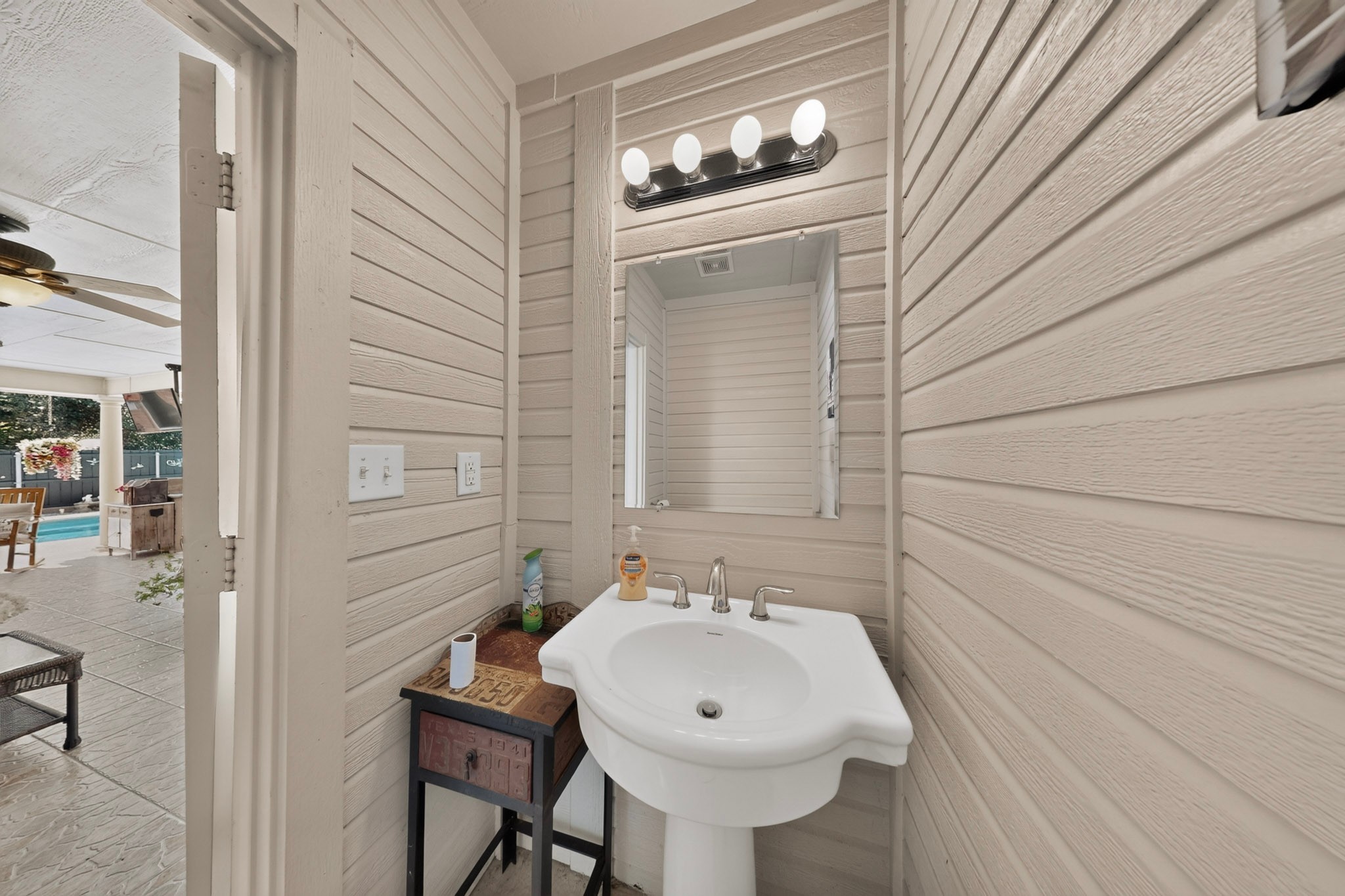 Bathroom with a white pedestal sink and vanity mirror beside an open doorway to the pool patio.