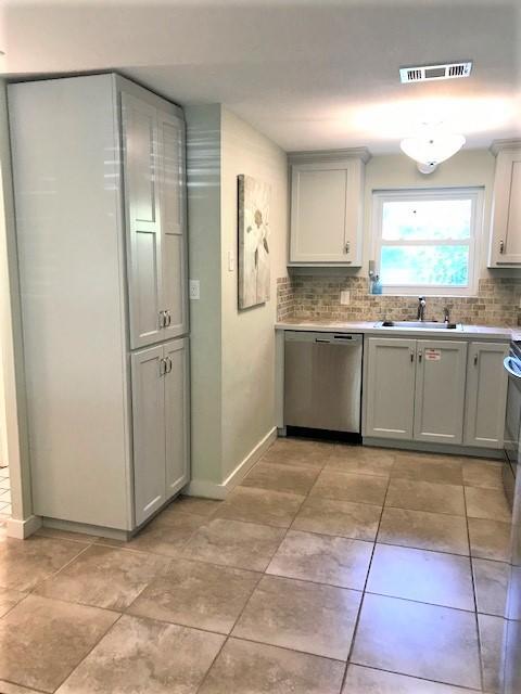Kitchen with gray cabinets, a window above the sink, and large tan floor tiles.