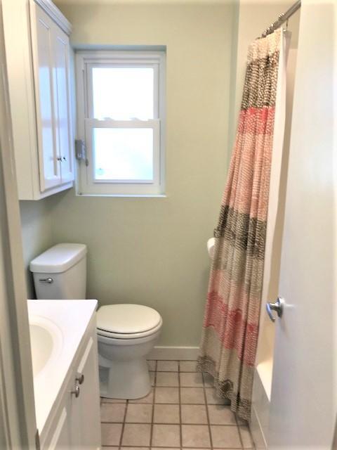 Bathroom with a white vanity and toilet, striped shower curtain, and tiled floor.