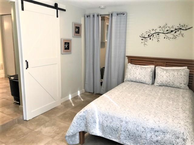 Bedroom with a patterned bedspread, wooden headboard, gray curtains, and a white sliding barn door.